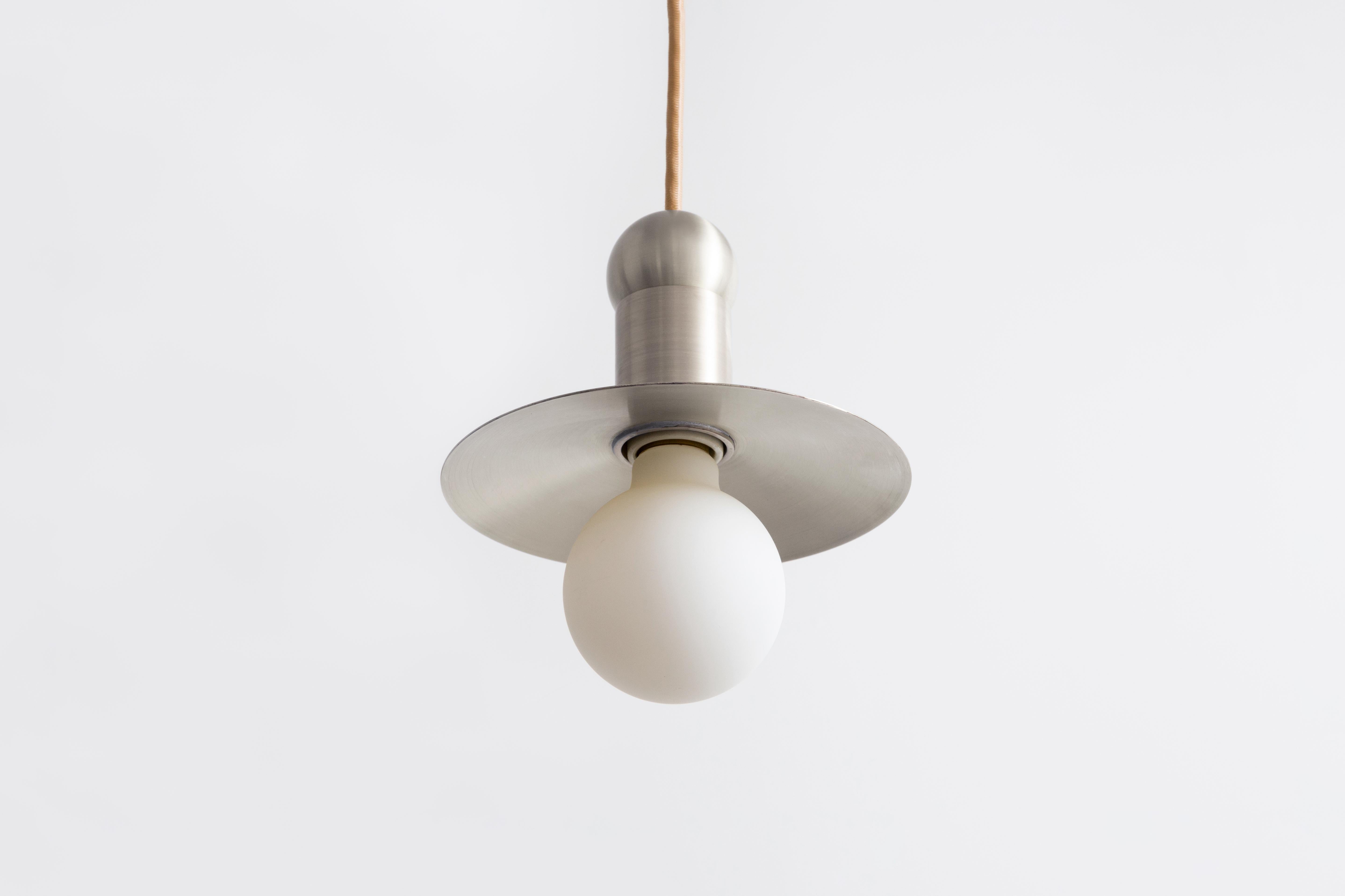 L'ORBIT CORD PENDANT place une seule ampoule incandescente contre une coupelle rayonnante stationnaire, explorant l'échelle et l'illumination d'une bougie des débuts de l'Amérique à travers la forme d'une suspension traditionnelle à éclairage vers