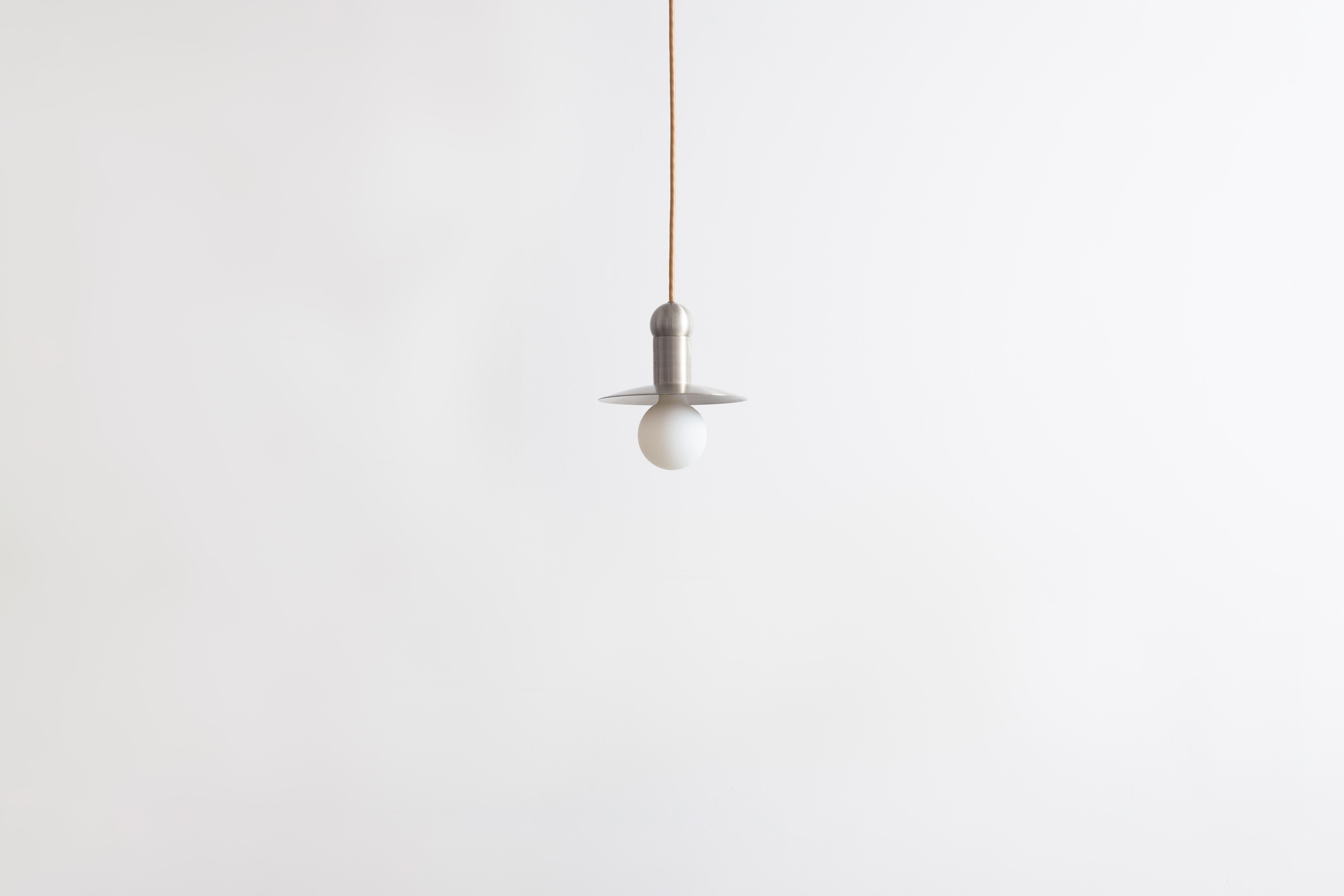 The orbit cord pendant positions a single glowing bulb against a stationary radiant dish, exploring the scale and illumination of an early American candle via the form of a traditional down-light pendant. With rotund details, each pendant provides a