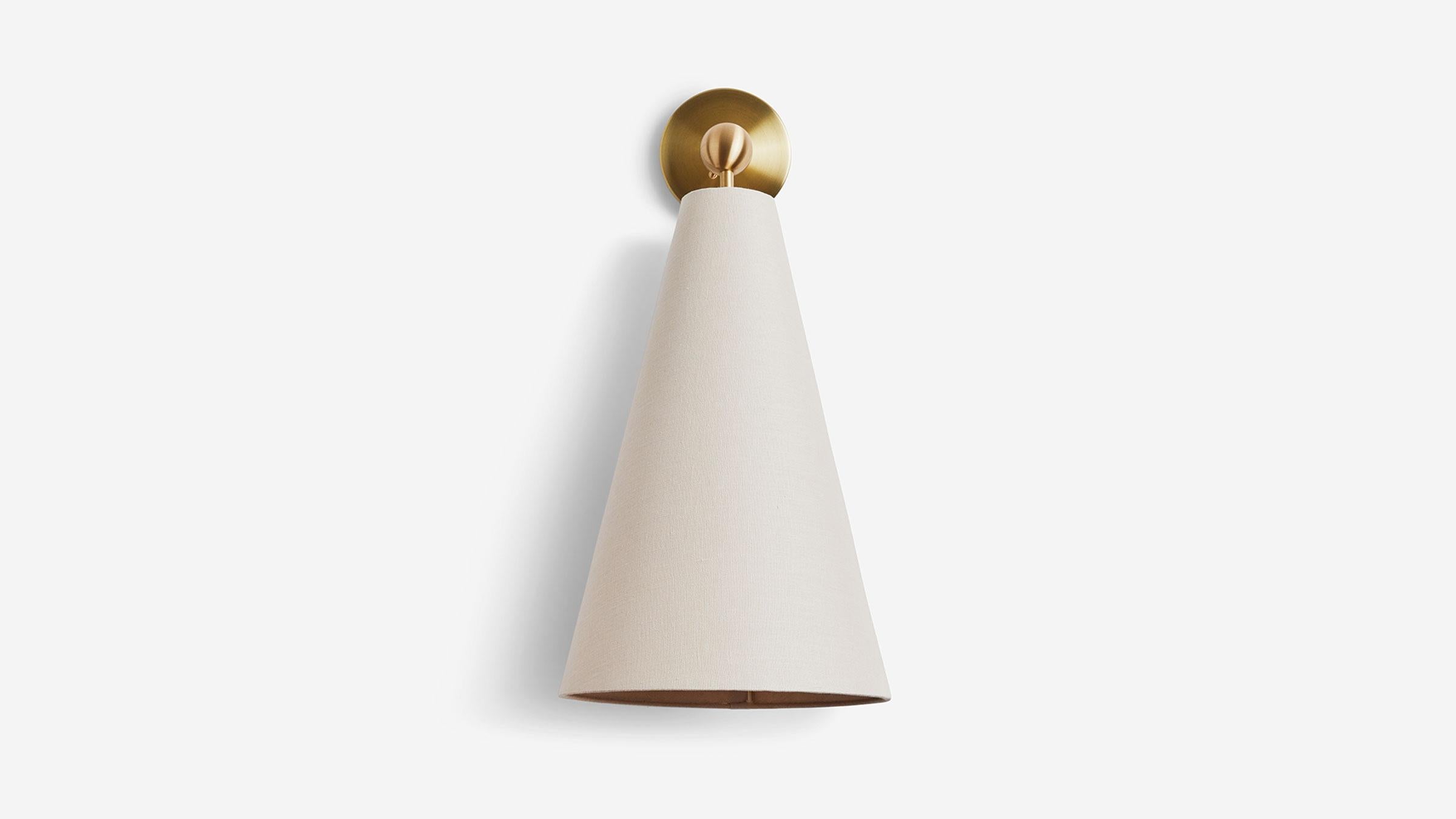 The Pendolo Sconce is composed of a directional fabric cone, radiating a subtle cast of light into a space - and a focused beam of light - in a myriad of configurations. Available in either Natural Burlap or Natural Linen, the cone form is expressed