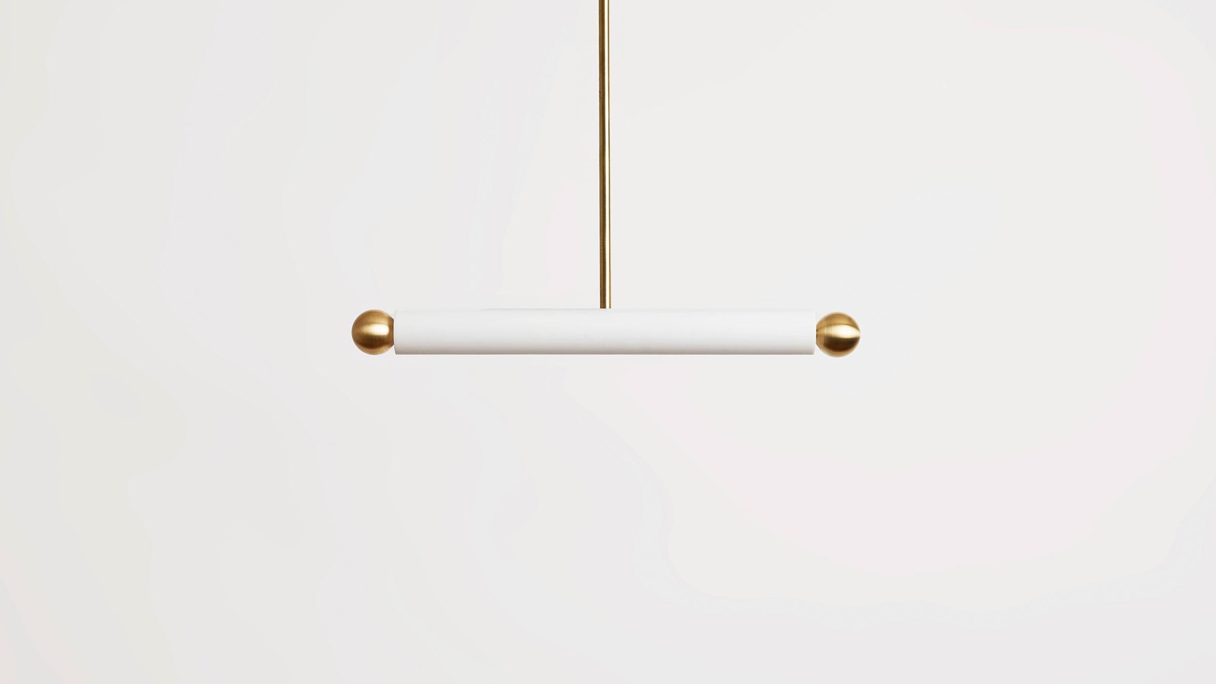 The tube pendant disperses a bold beam of light into space, hovering delicately above a counter, table, or hall. Matte blown-glass is playfully offset by two metal balls, presenting a fixture that is both luminous and rhythmic. Made in the USA. UL