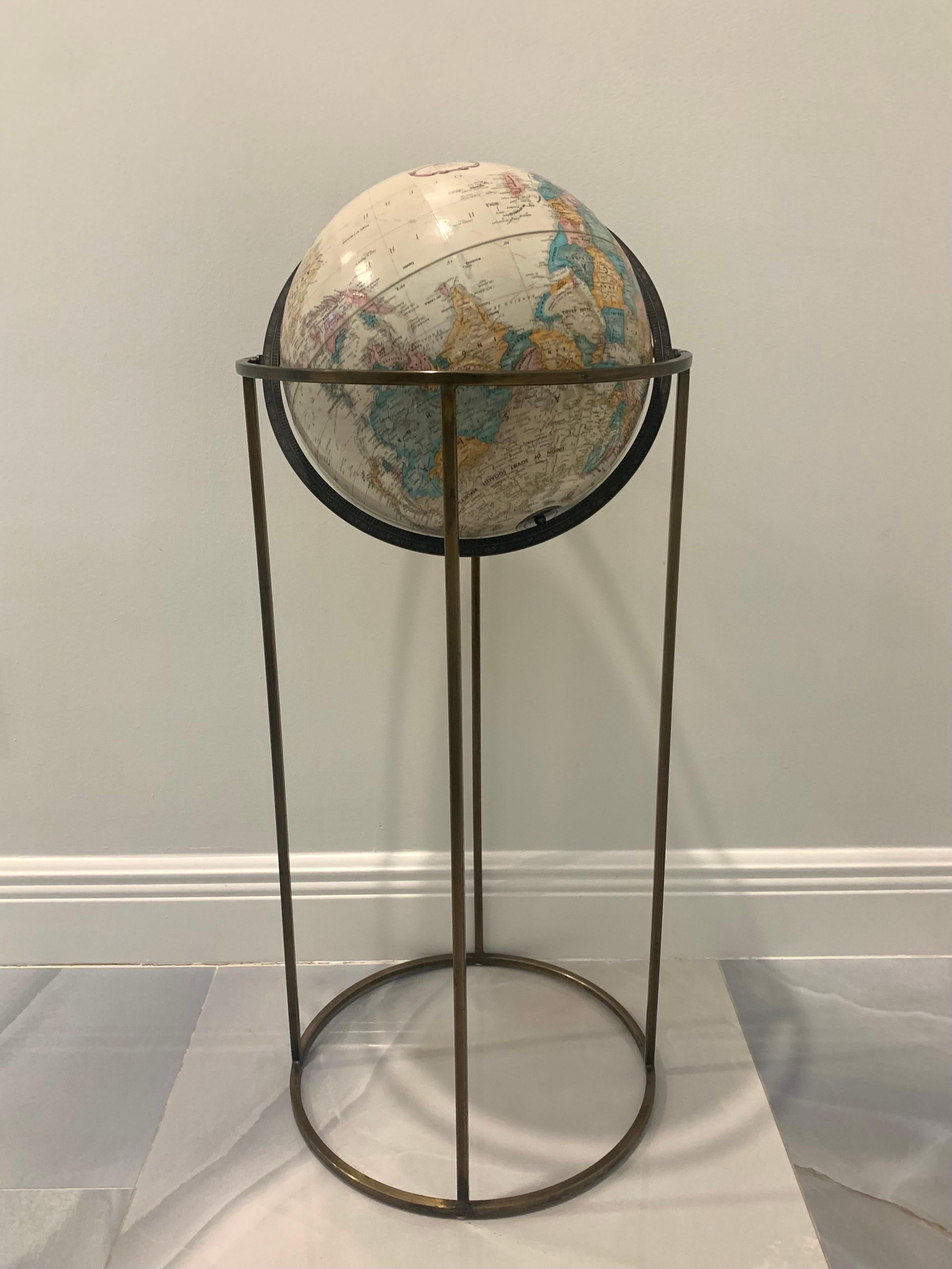 World globe by Replogle in the style of Paul McCobb. Made in the USA circa 1970s. Signed. 

Beige globe with textured topography. Supported by a swivel stand in antiquated brass. Featuring square tube design made popular by McCobb. 

