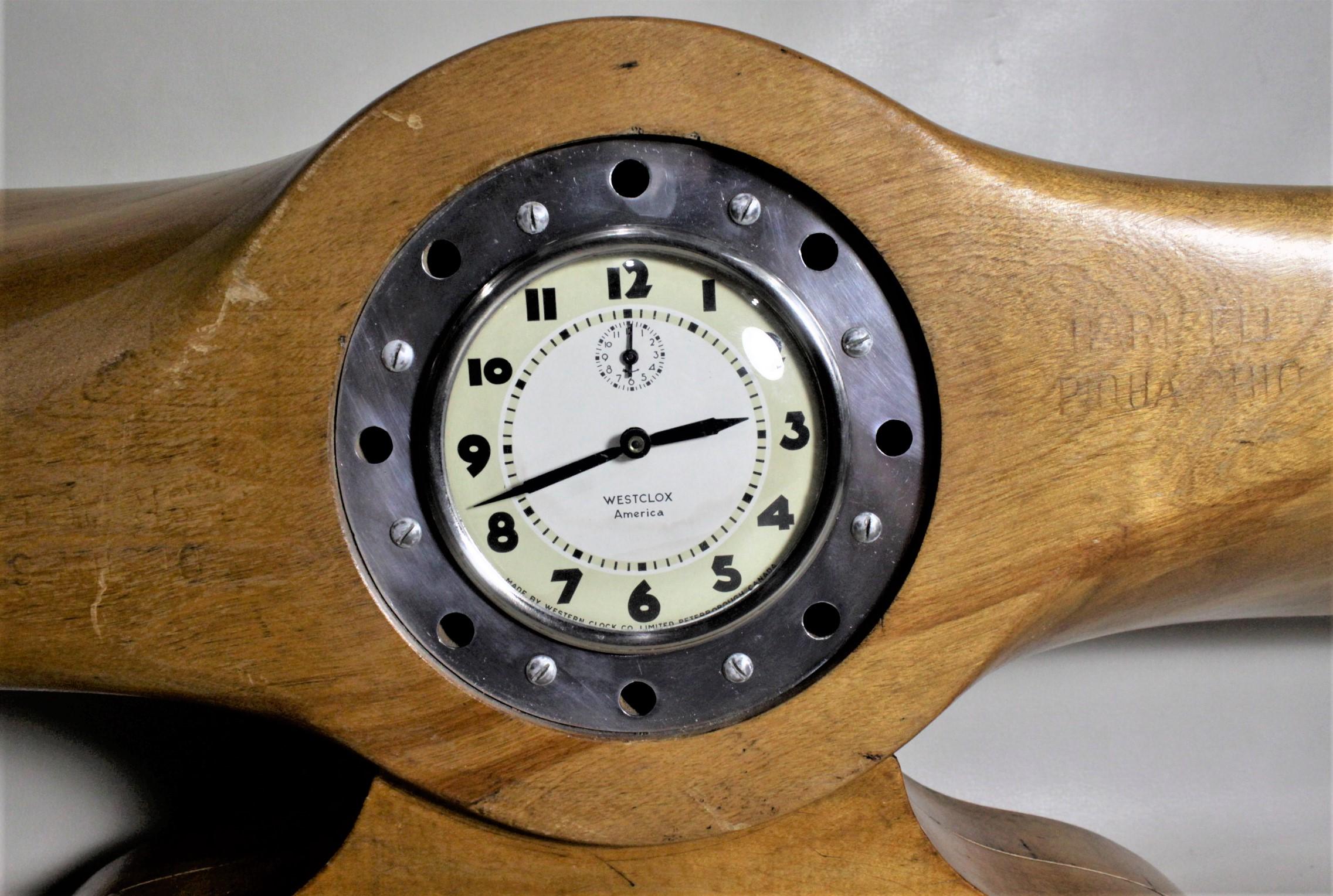This wooden Folk Art made propeller clock is presumed to have originated in England and fashioned into a mantel clock in North America in circa 1960. The propeller has been cut and a wooden base added and a hand wind clock movement added to produce