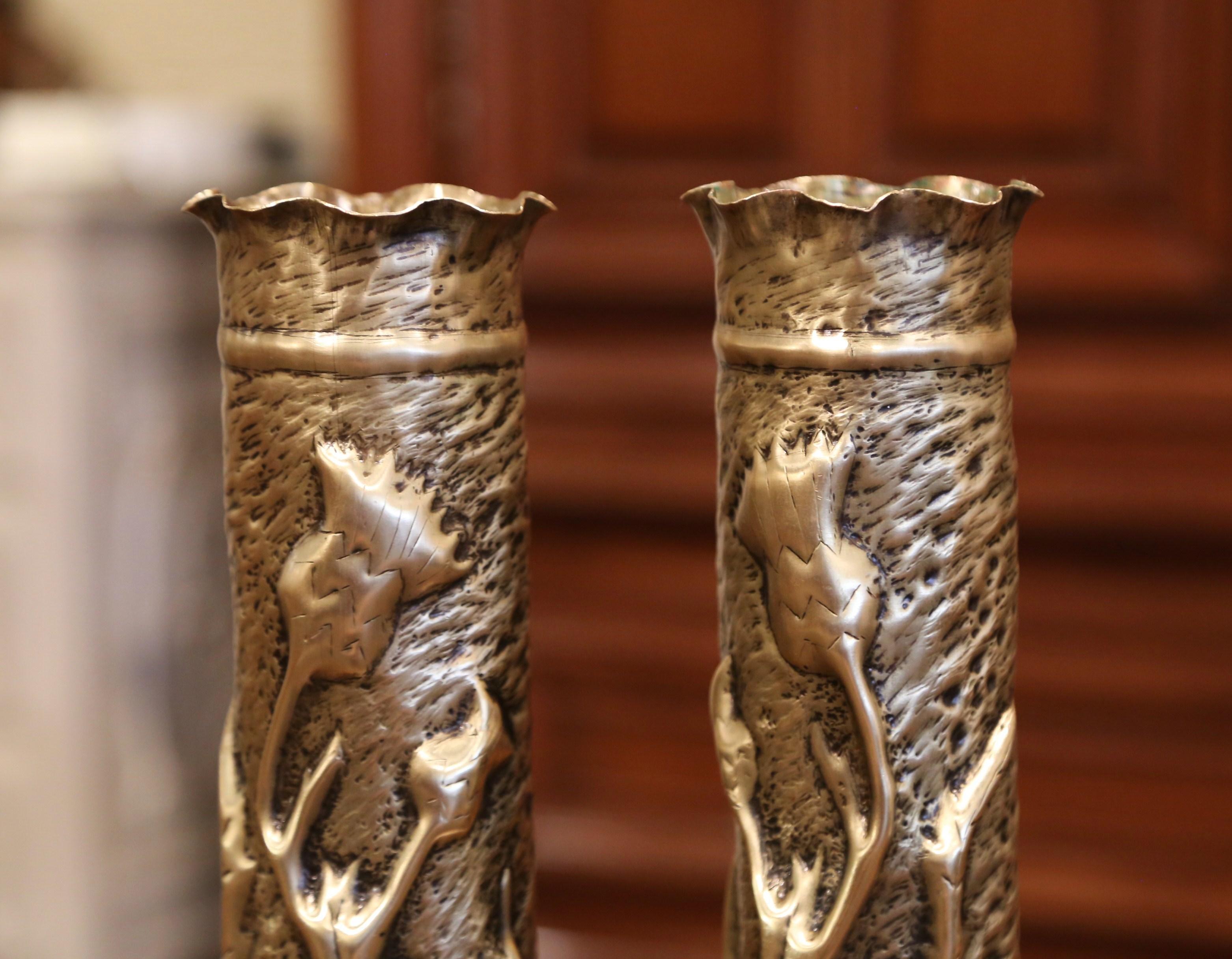 Decorate a man's office or a study display shelf with this pair of antique trench art shell vases from France, circa 1915. Made of brass, the artillery shell casing vases feature repousse floral and leaf decor over a scalloped top rim. Both WWI