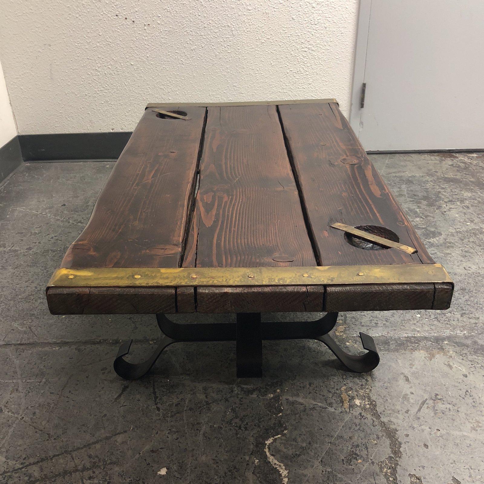 A magnificent restoration of a World War II liberty ship hatch cover lovingly re-purposed into a finely finished coffee table with an iron twin pedestal base. Bronze hardware on the edges and corners of the tabletop are expertly installed. The