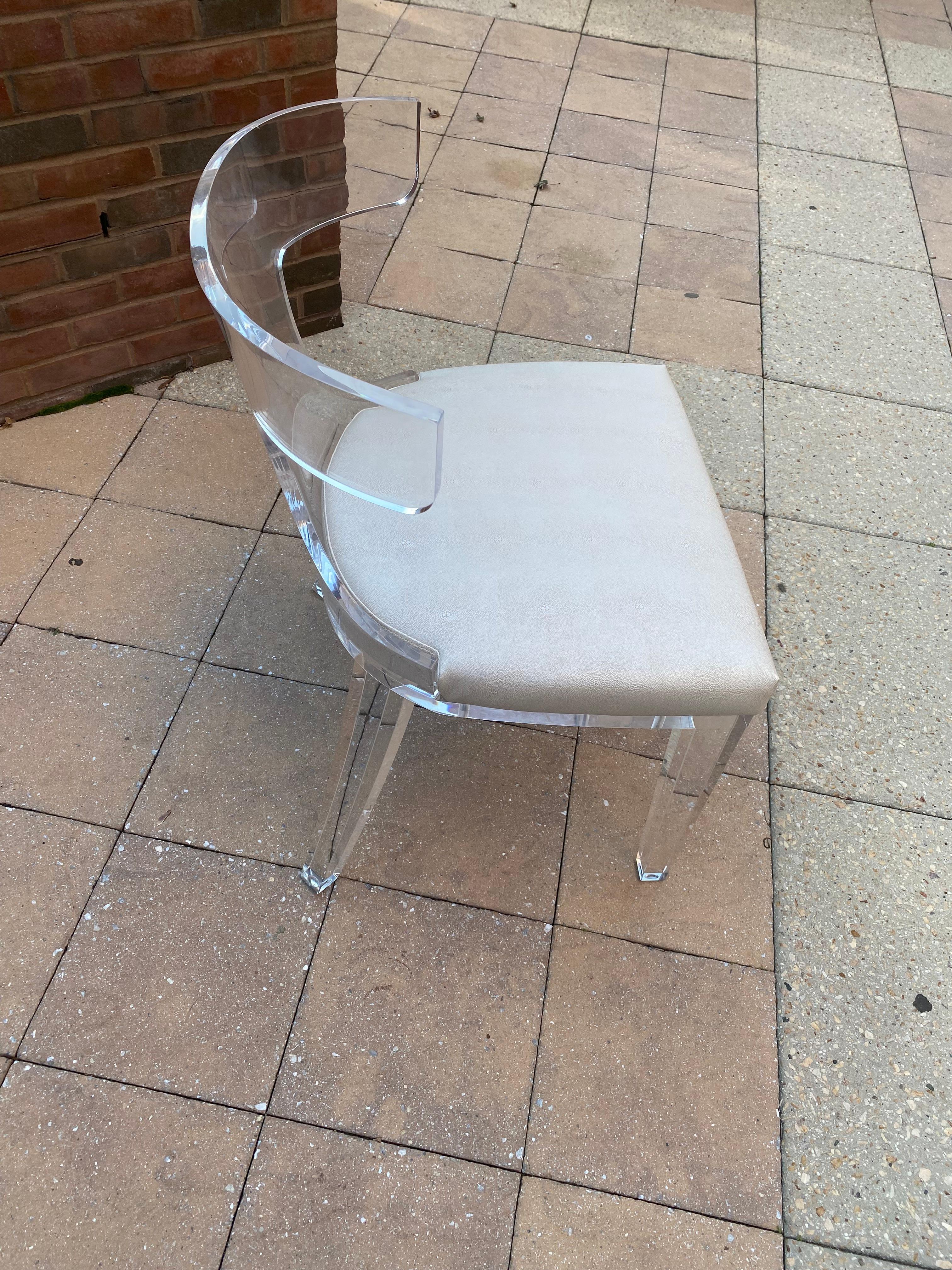 Striking chair modeled after the iconic classic Greek Klismos chair.  This sturdy and well weighted transparent acrylic chair features a curved back, tapered legs and a seat upholstered in a beige faux shagreen. 


