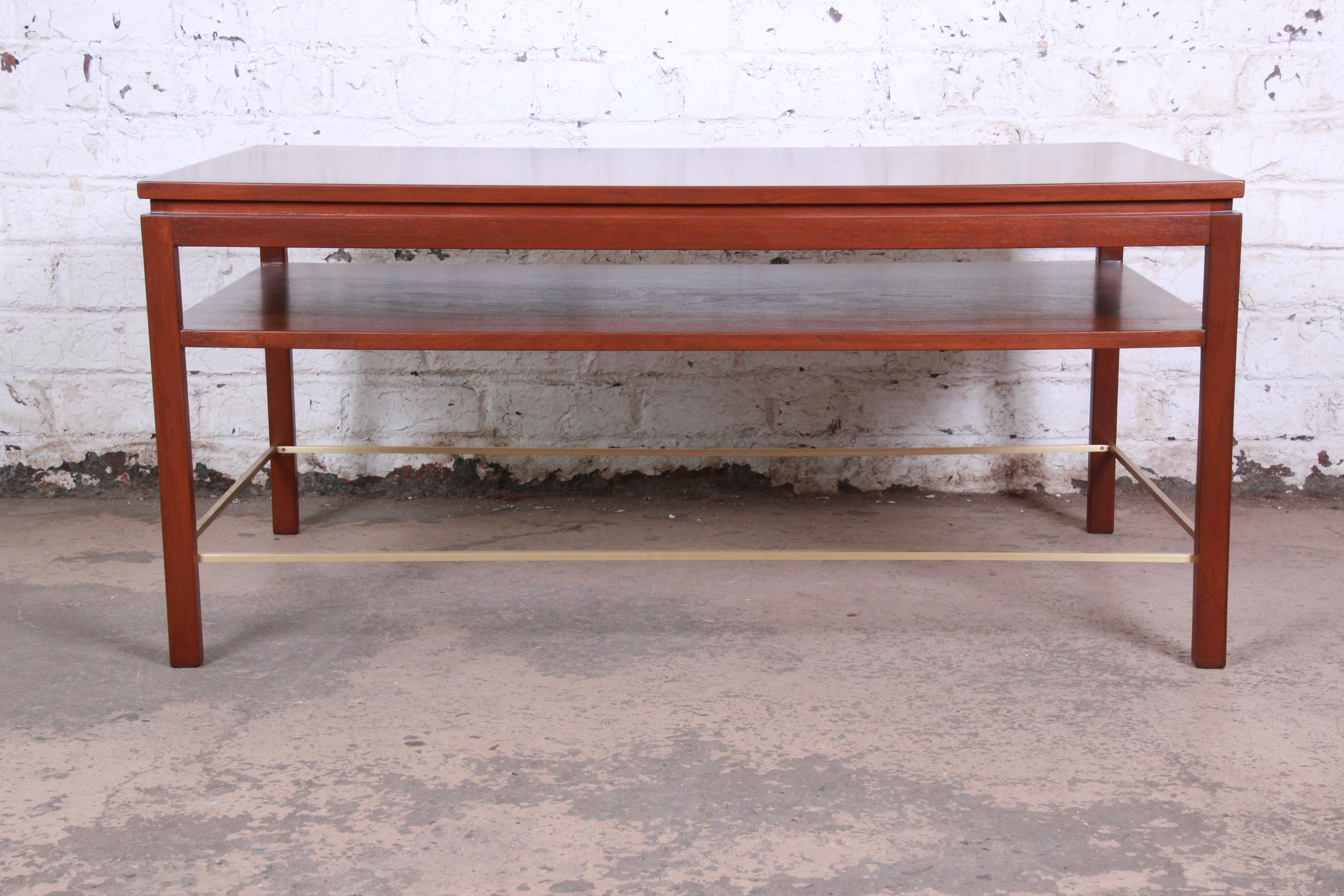 An exceptional Mid-Century Modern two-tier walnut and brass cocktail or coffee table designed by Edward Wormley for Dunbar Furniture. The table features gorgeous walnut wood grain and sleek, Minimalist mid-century design. Brass stretchers accent the