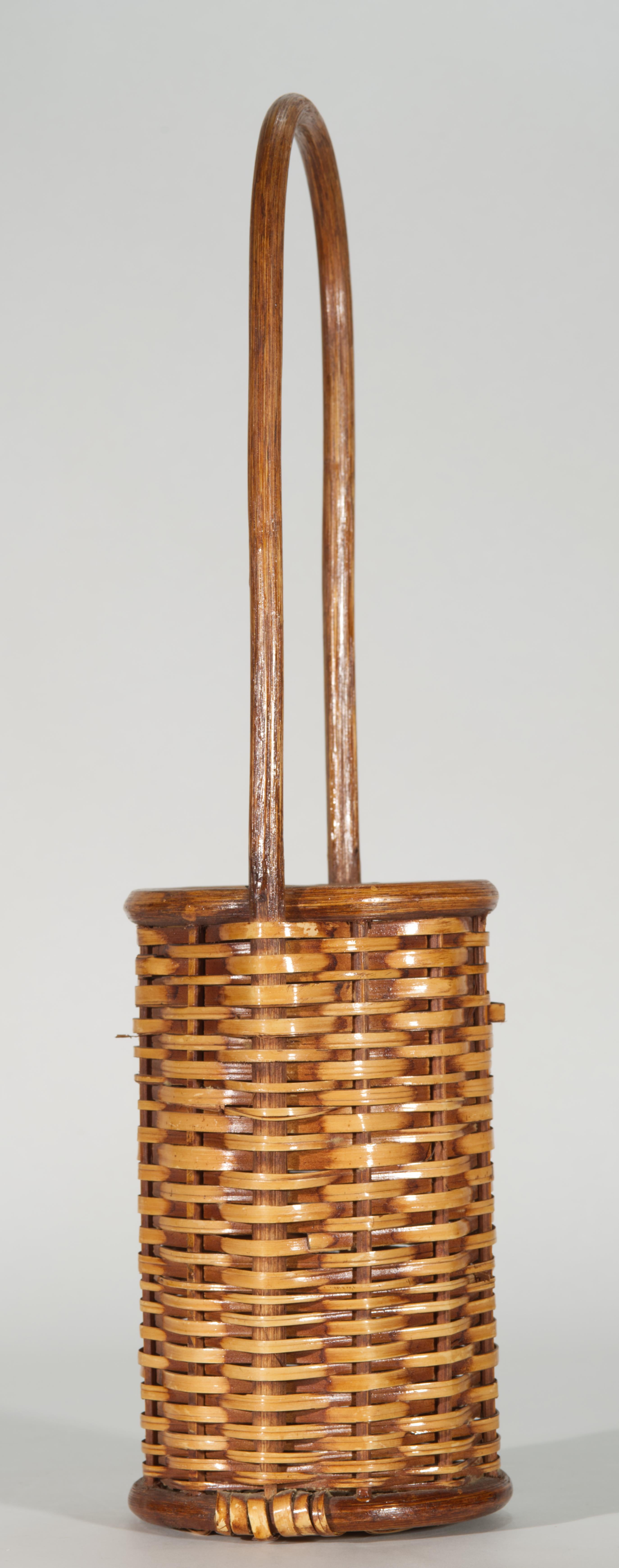  Le panier ouvert de l'Art of Vintage des Philippines présente un corps cylindrique allongé et une poignée proéminente. Le corps est tressé en trame serrée selon un motif simple ; les fibres sont assombries par la fumée. La coloration à la fumée