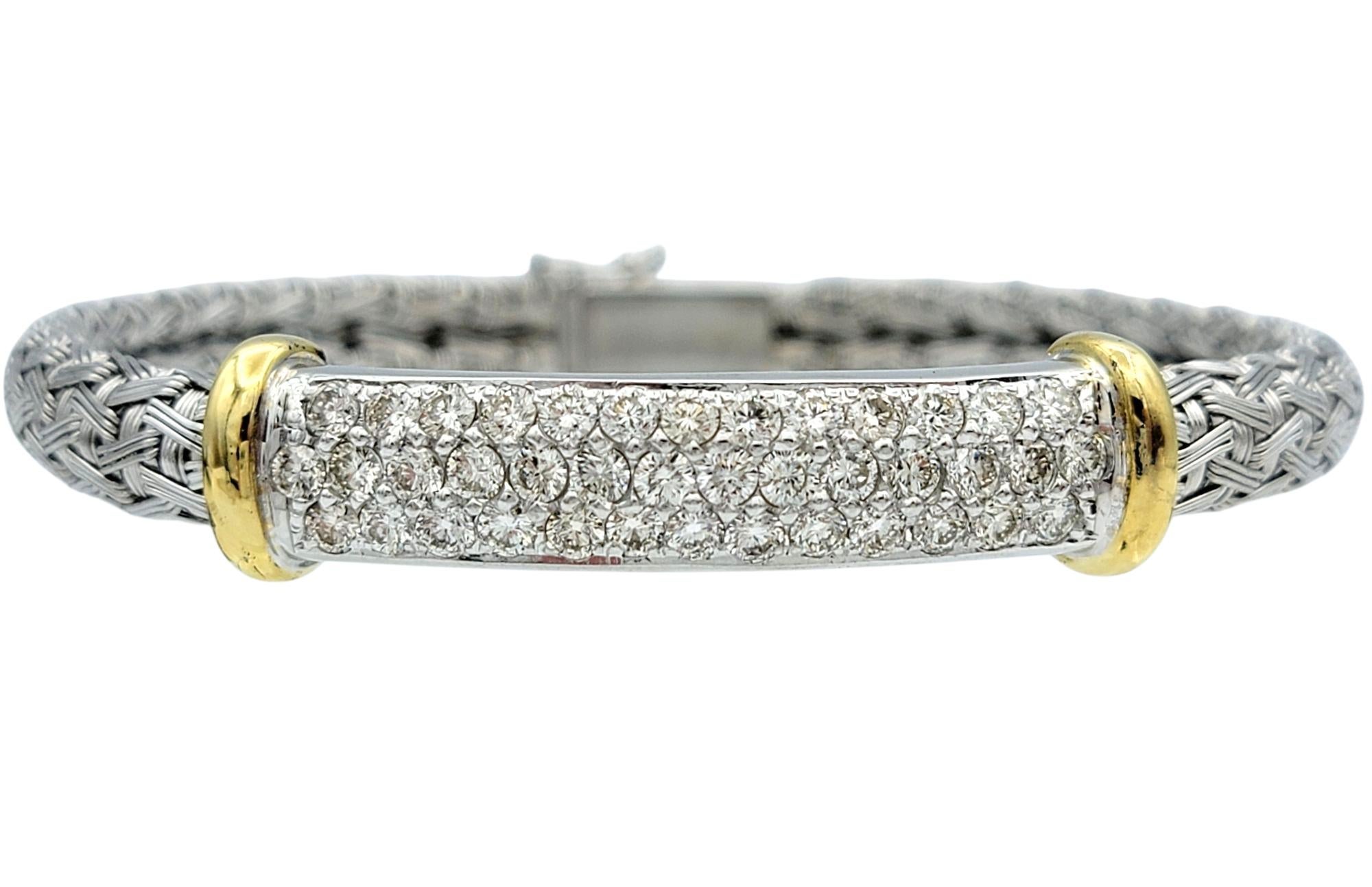 This diamond woven bangle bracelet offers a masterful mix of metals and textures, blending the cool tone of 18 karat white gold with the warmth of 18 karat yellow gold accents. The bracelet features a tightly woven design that feels both intricate