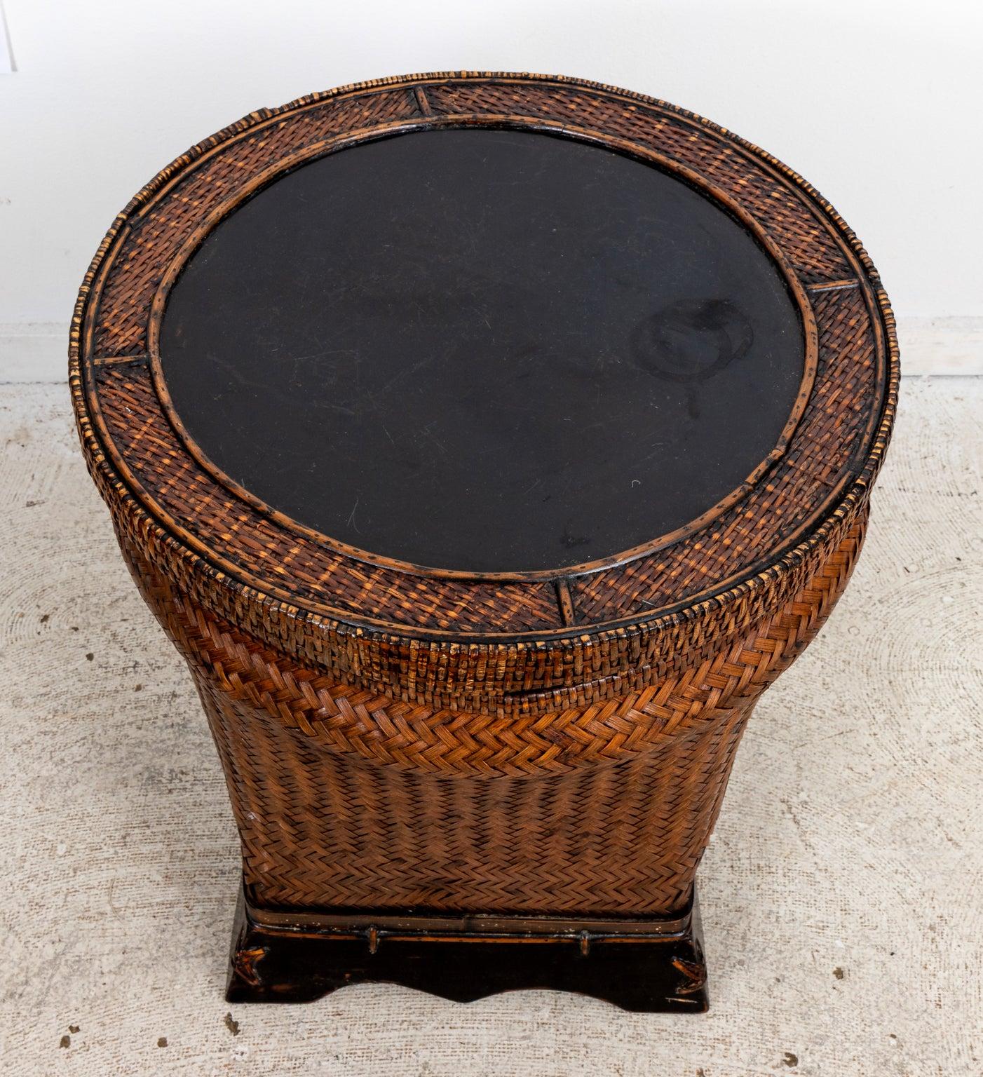 Circa 1960s round woven wicker and rattan basket side table in the Hollywood Regency style with black lacquer lid that lifts off to provide storage. Made in China. Please note of wear consistent with age including a few dents on the black painted