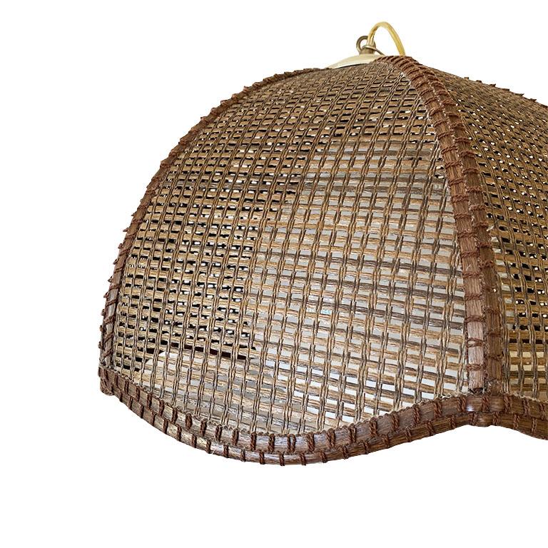 A lovely Bohemian scalloped edge wicker or cane swag pendant light. Woven brown fibers of wicker, bamboo, or rattan are woven together around a white glass globe. A gold chain attaches with a plug and switch. This would be a fantastic touch to a