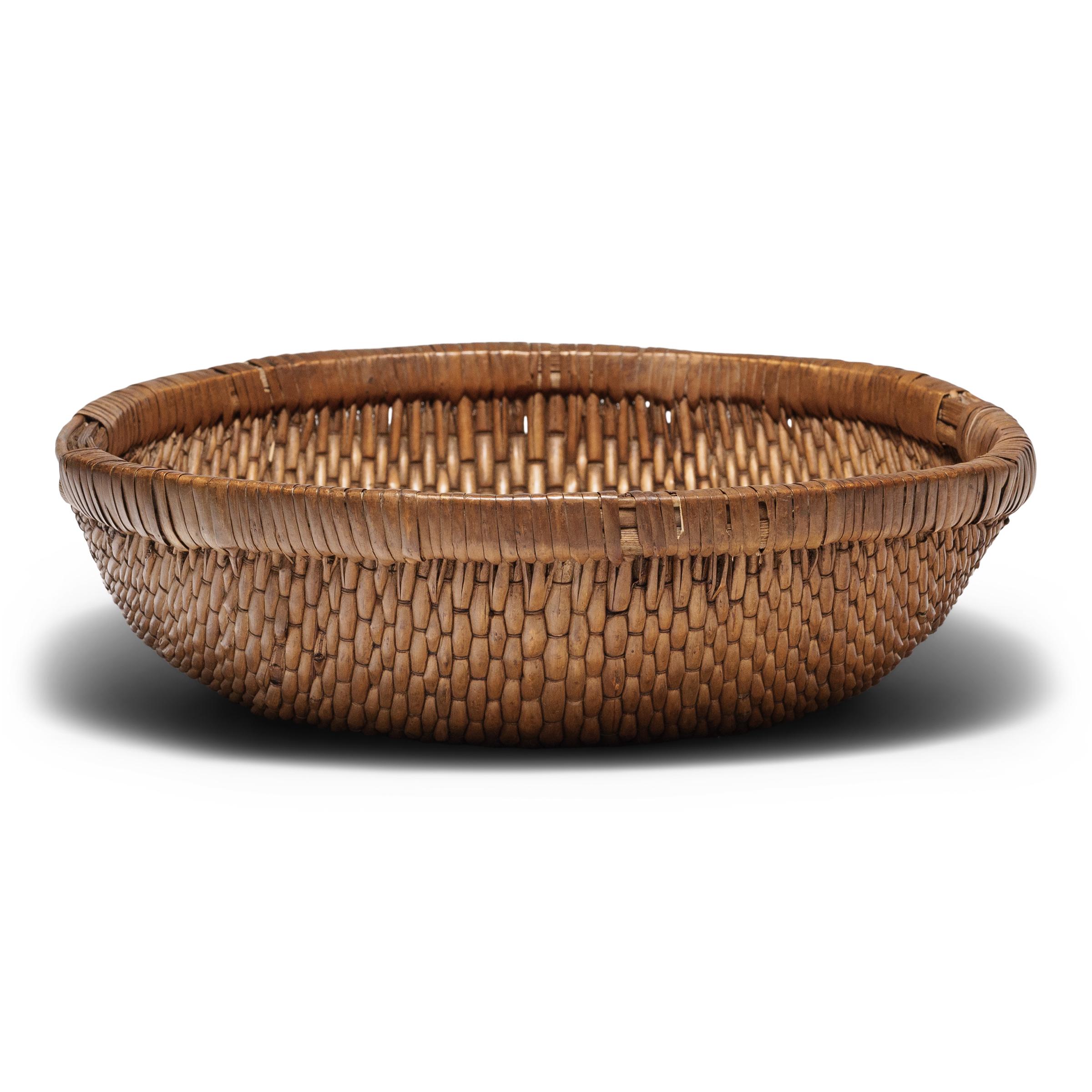 This round woven tray basket was originally used for harvesting grains or as a kitchen vessel for food prep and storage. Despite its humble origin, the basket exhibits remarkable workmanship, beautifully woven by hand of willow and cord around a
