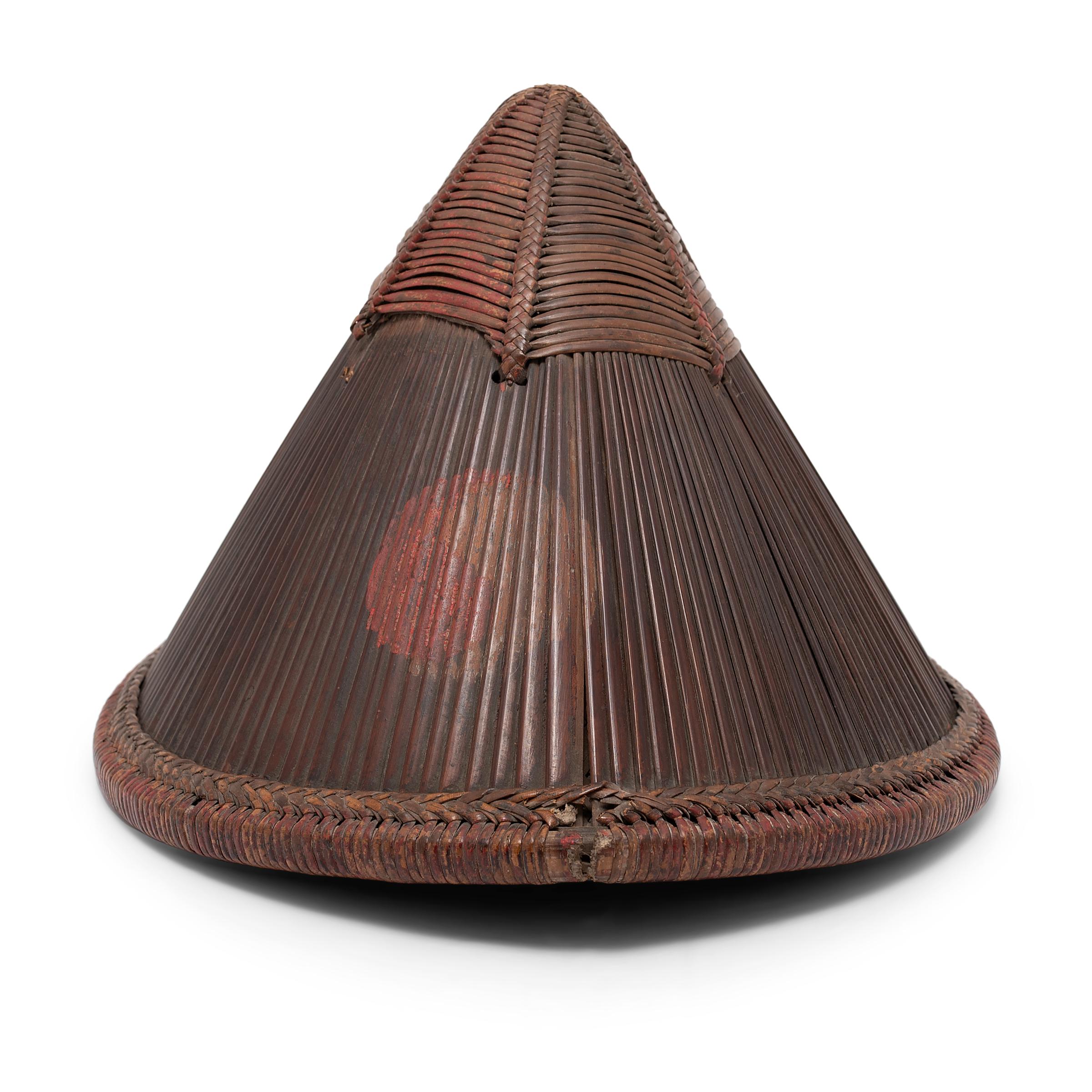 Dieser konische, geflochtene Hut stammt aus dem China des 19. Jahrhunderts und wird fachmännisch ganz aus Bambus gefertigt. Die Außenseite besteht aus mit Rattanstreifen geflochtenen Bambussplittern, die durch eine Innenauskleidung mit einem