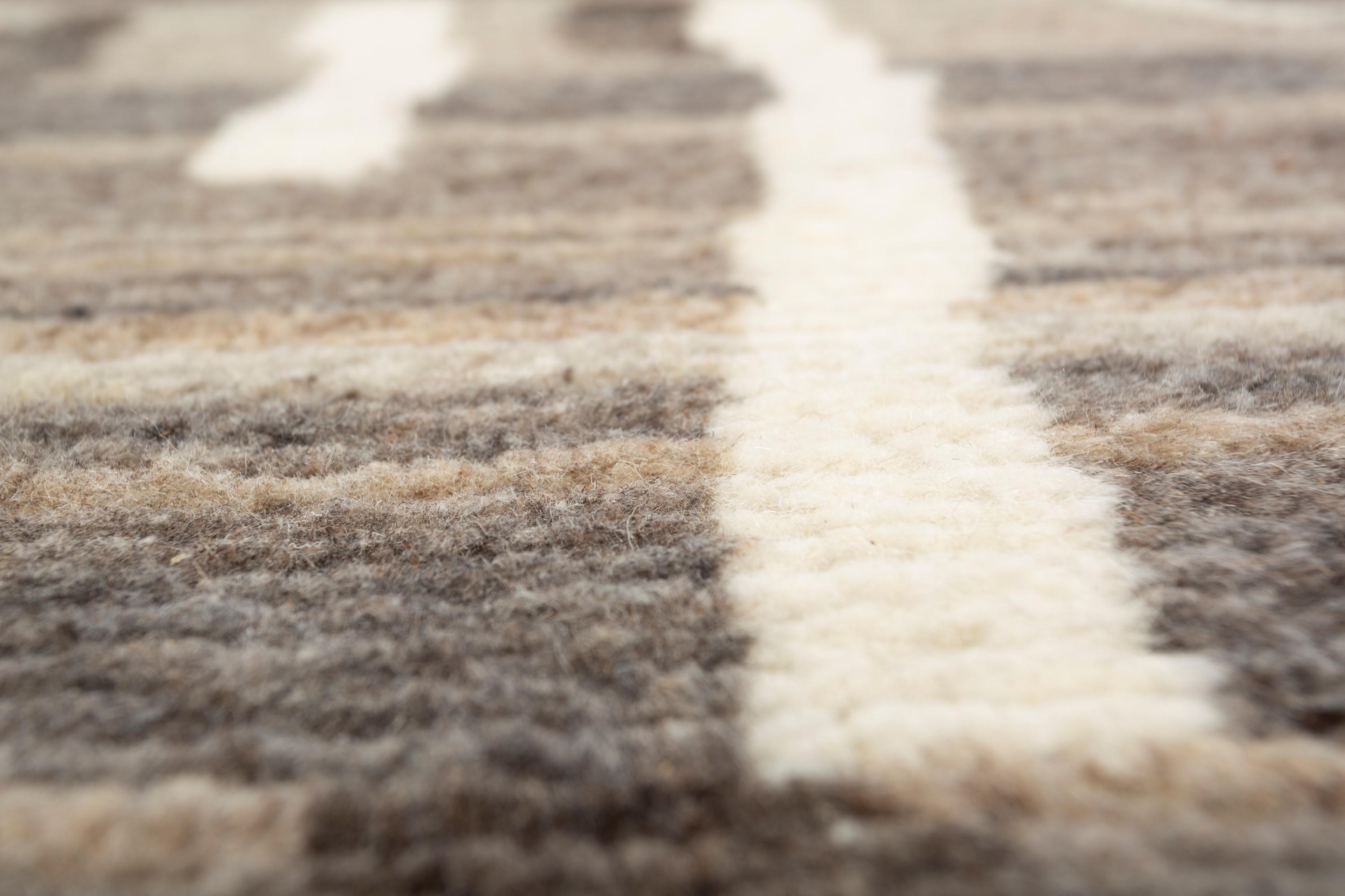 The modern wool rug is a captivating blend of eclectic patterns and natural elegance, hand-knotted in the heart of rural India using the finest all-wool construction. This stunning rug boasts a natural gray ground, reminiscent of the desert sands,