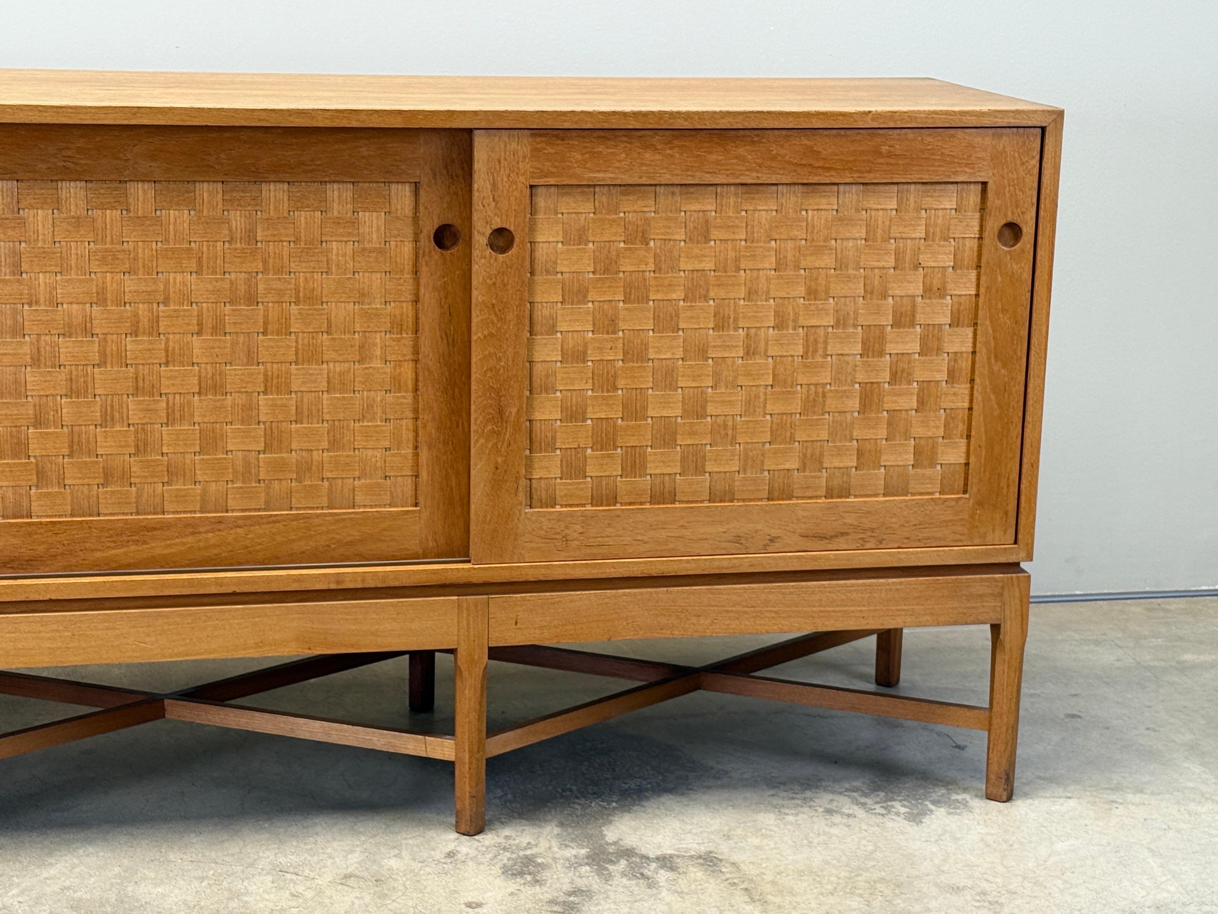 A rare woven front sliding door cabinet designed by Ilse Rix for Uldum Møbelfabrik. Beautifully constructed with a nice even warm patina to the Oak. Some drawers are leather lined. 