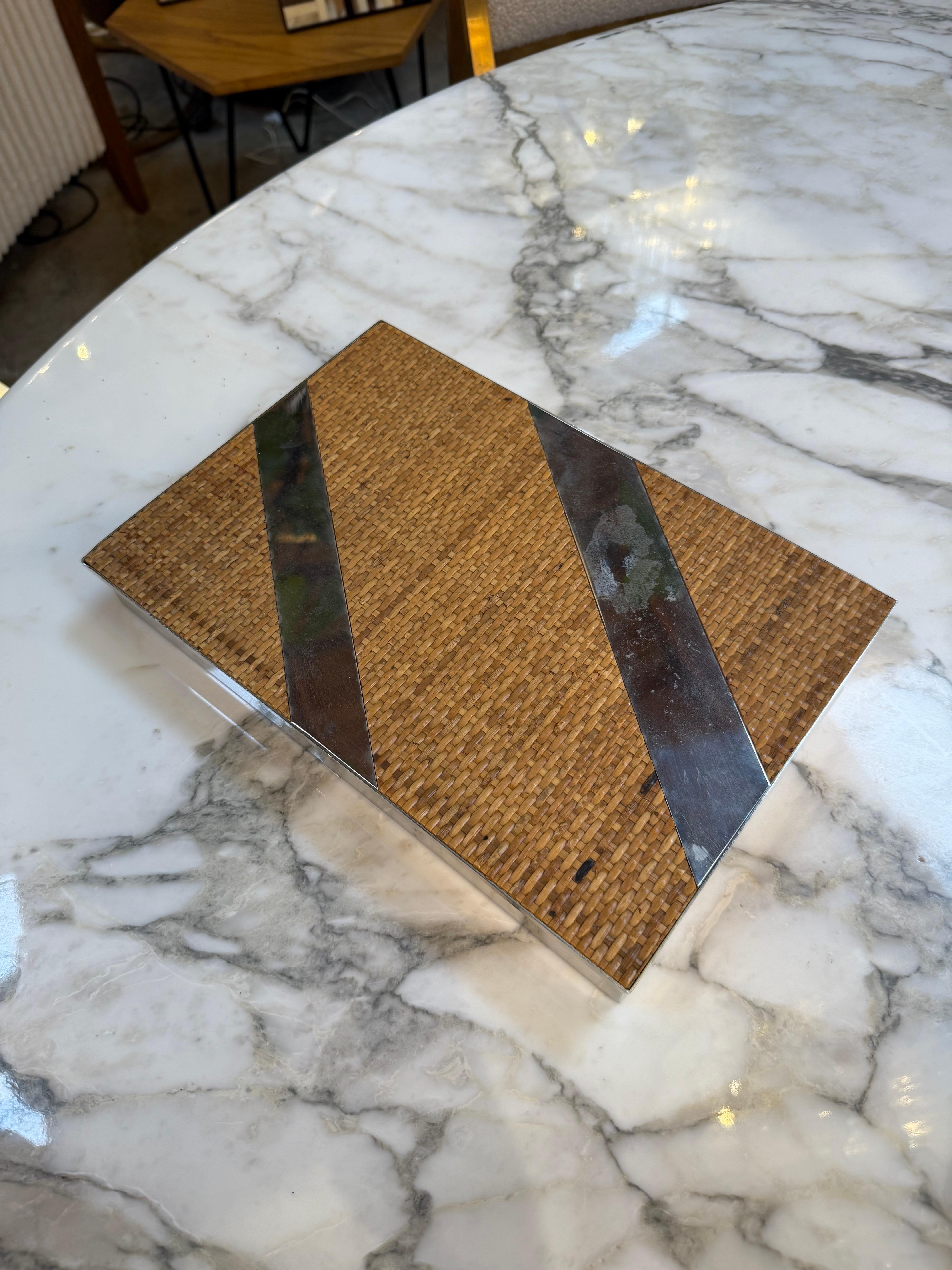 This sophisticated mid-century rectangular box features a beautifully woven rattan surface accented with bold diagonal chrome inlays, creating a striking balance between natural texture and sleek metallic contrast. The craftsmanship highlights the