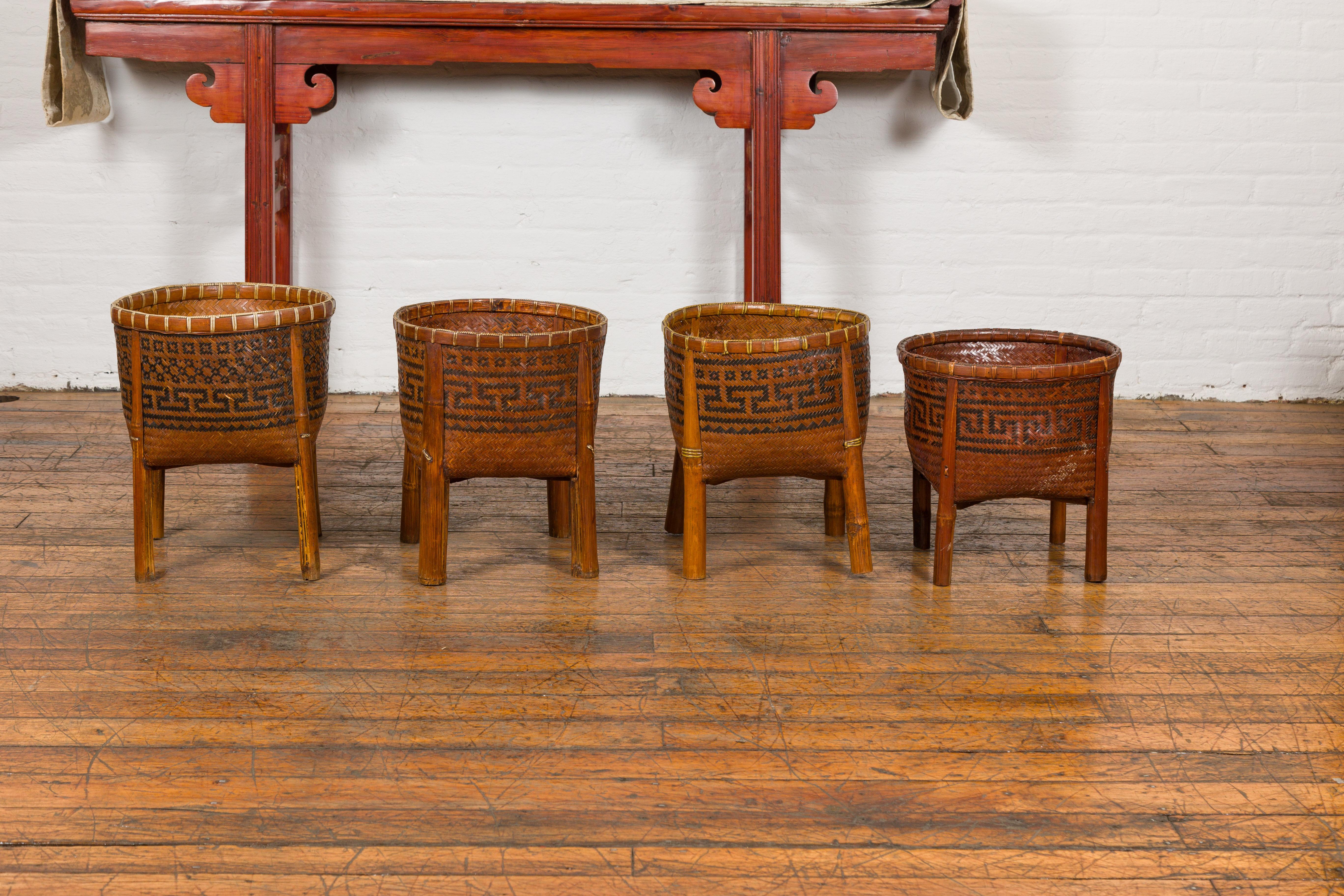 Old woven rattan rustic Chinese baskets on wooden legs, with Greek key friezes. Imbued with rustic charm and historic elegance, these vintage Chinese baskets are charming artifacts from a bygone era. Handwoven from sturdy rattan, they captivate with
