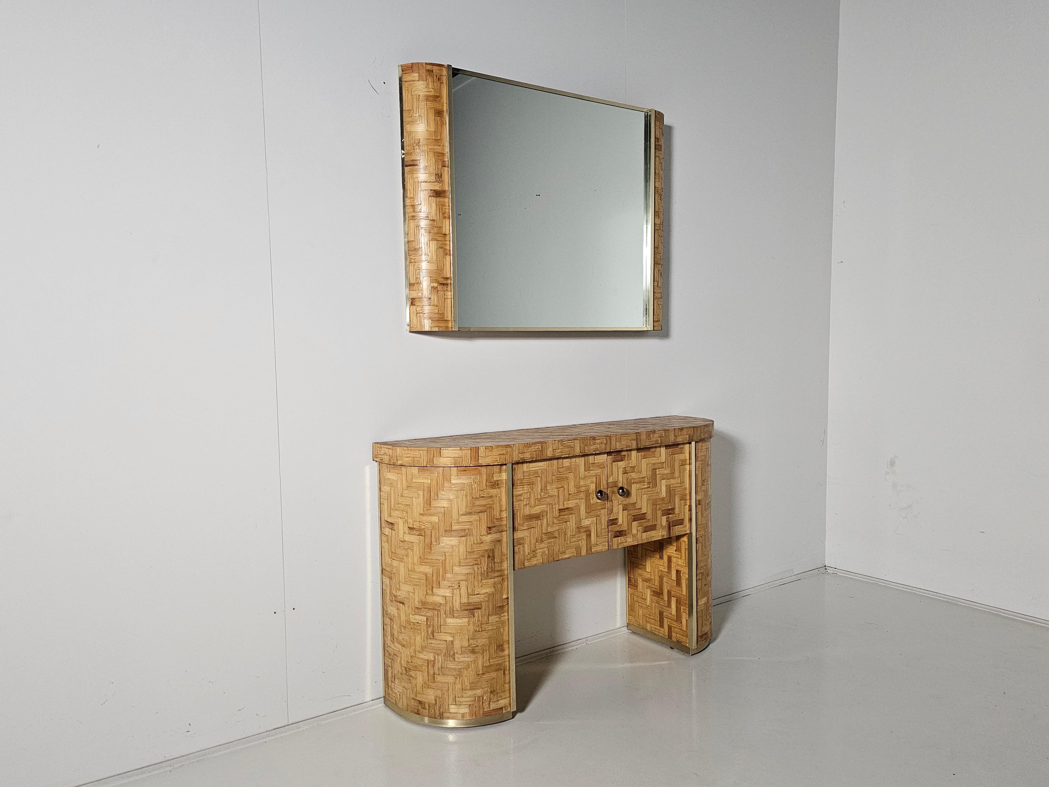 Hollywood Regency brass and rattan console/vanity table with matching mirror from Italy. Made in the 1970s.

Made of plywood covered with a dense weave of rattan blocks and brass details embellish and create glamorous details. The style of this set