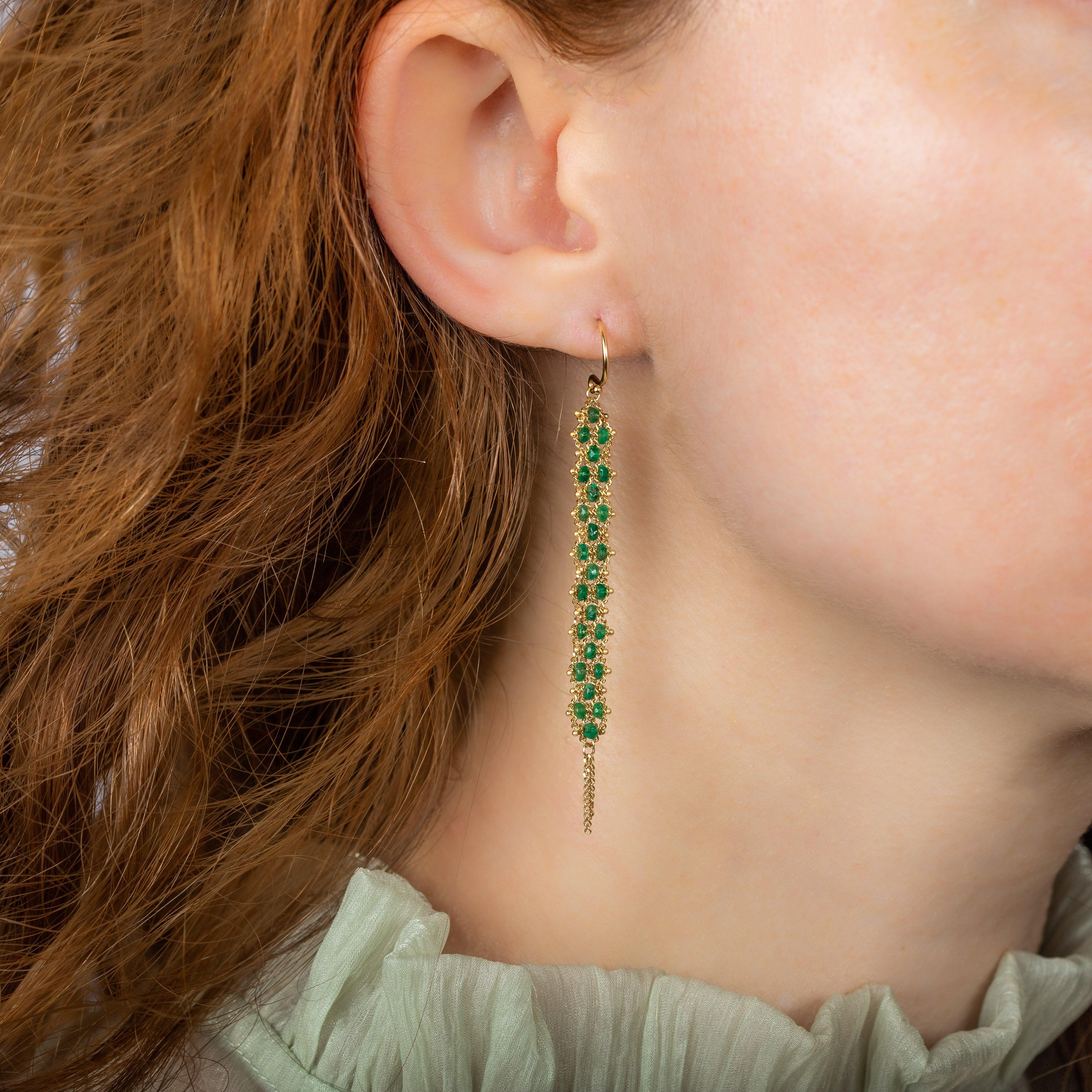 These earrings shimmer with a verdant swath of lush green Emeralds that have been meticulously hand-woven into 18K yellow gold chains to achieve a textile-like effect. The result is long and flexible, with a short burst of gold chain cascading off