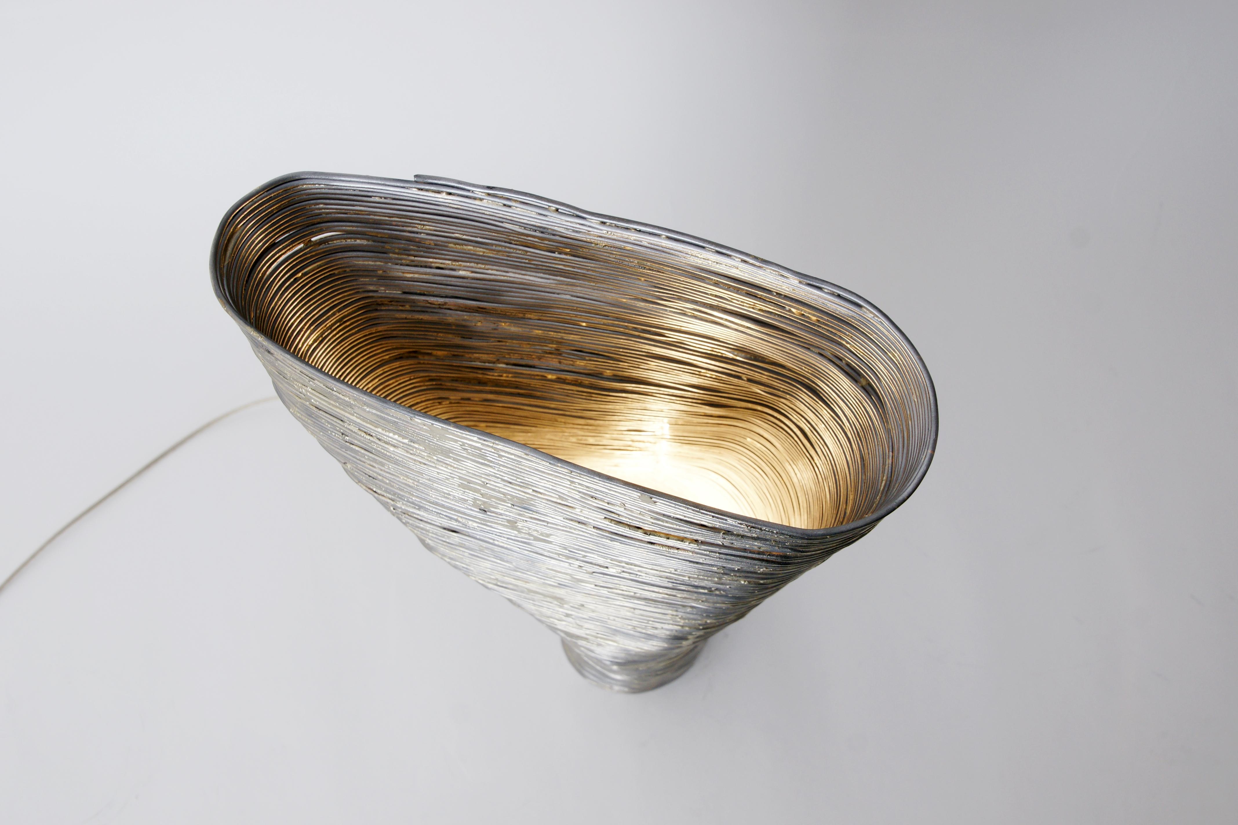 Lampe de table en acier Beeche de Johannes Hemann
MATERIAL : Fil d'acier, laiton
Dimensions : hauteur 50cm, Ø 12- 20cm

'Wrap, la série d'objets du designer allemand Johannes Hemann examine les coquilles des choses qui restent après leur