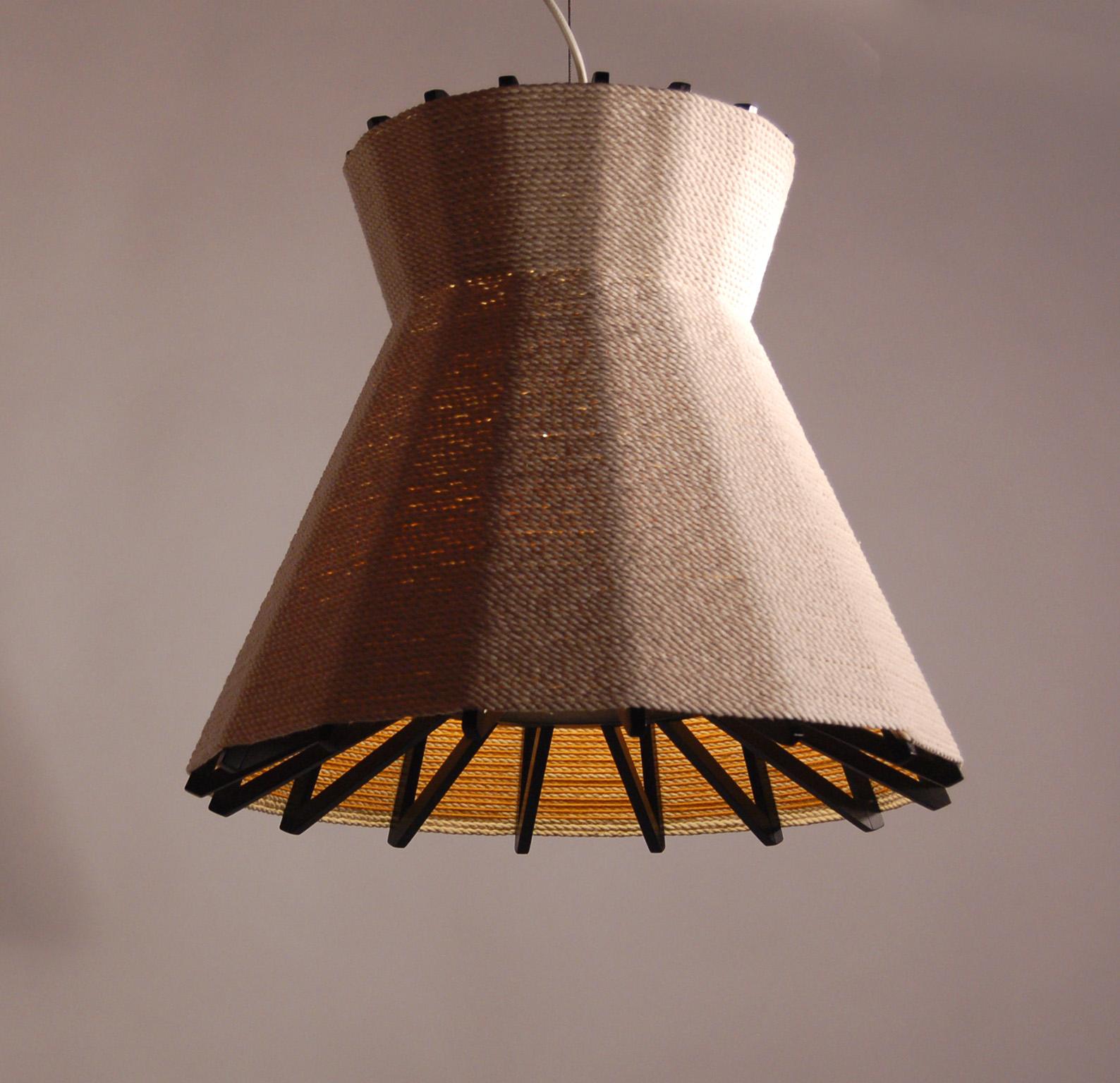 The wrapped lamp combines the warmth of cotton and wool around an exposed blackened wood frame to create a miniature roof canopy. The shaded down light creates an intimate scene above a dining table. Standard fixture comes with interior accents of
