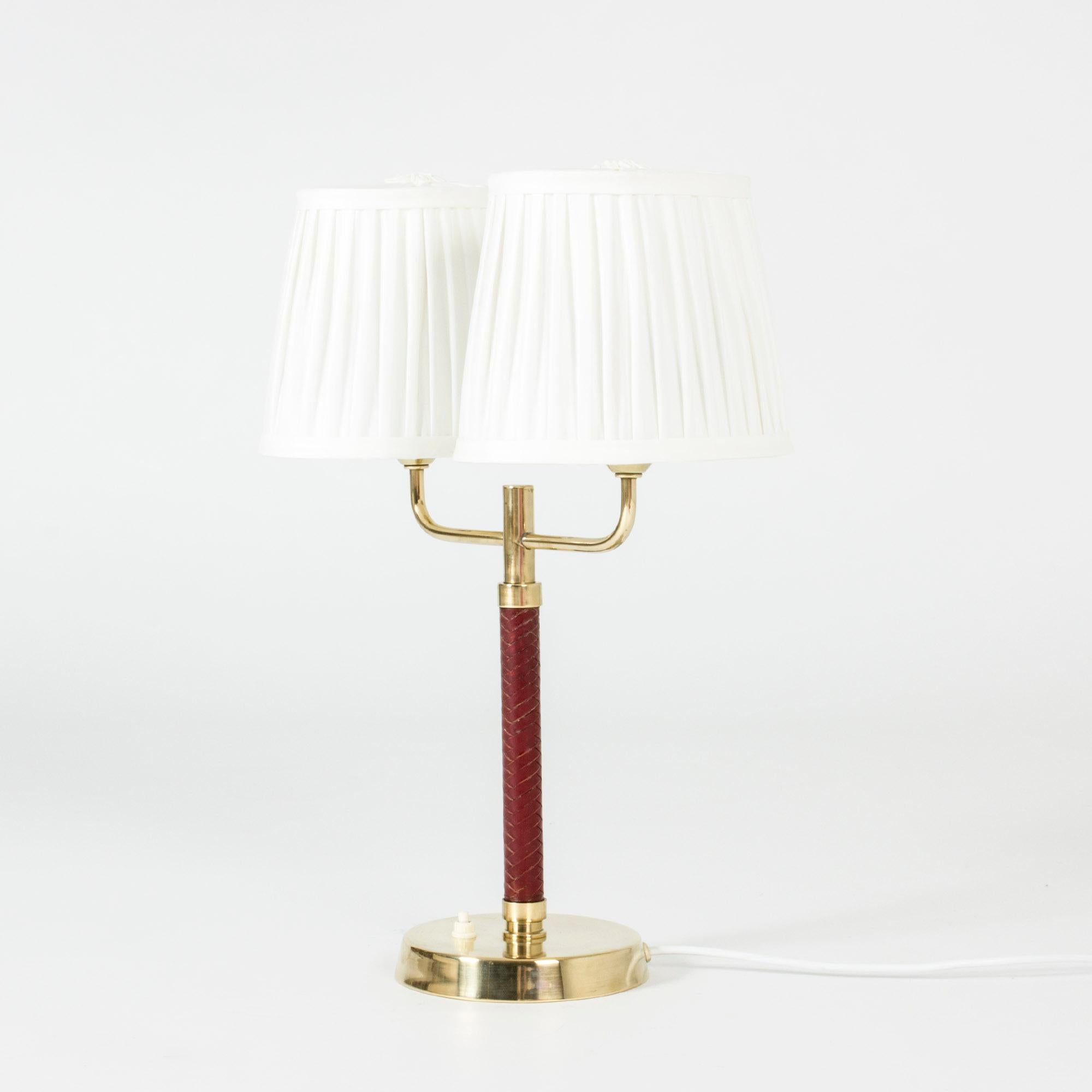 Elegant table lamp from Karlskrona Lampfabrik, made from brass with an oxblood red wreathed leather handle. Double lampshades made from pleated white fabric.