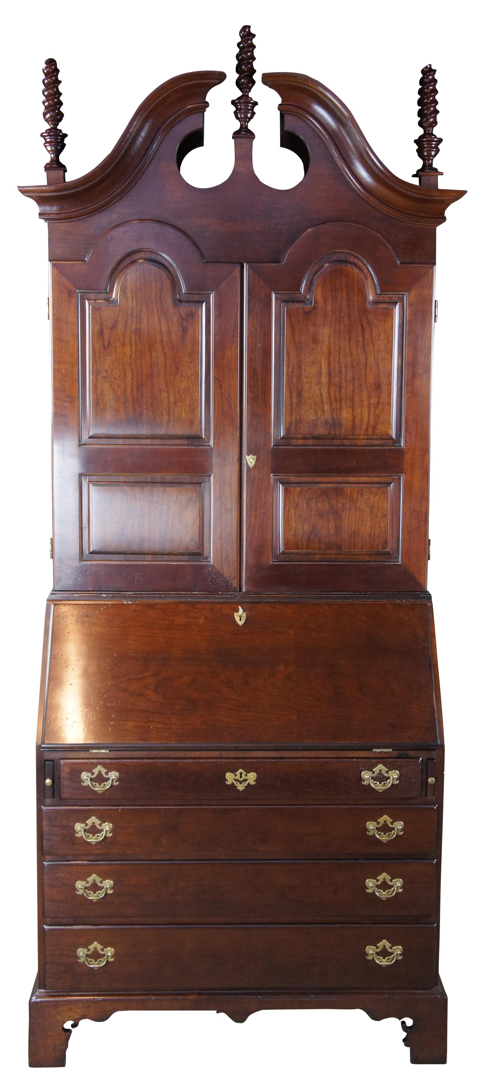 A Monumental New England style secretary desk from Wright Table Company. Made from solid cherrywood and veneers. Features a broken pediment with three flame turned trophy finials. The arched doors open to pigeon holes, shelves and a raised scalloped