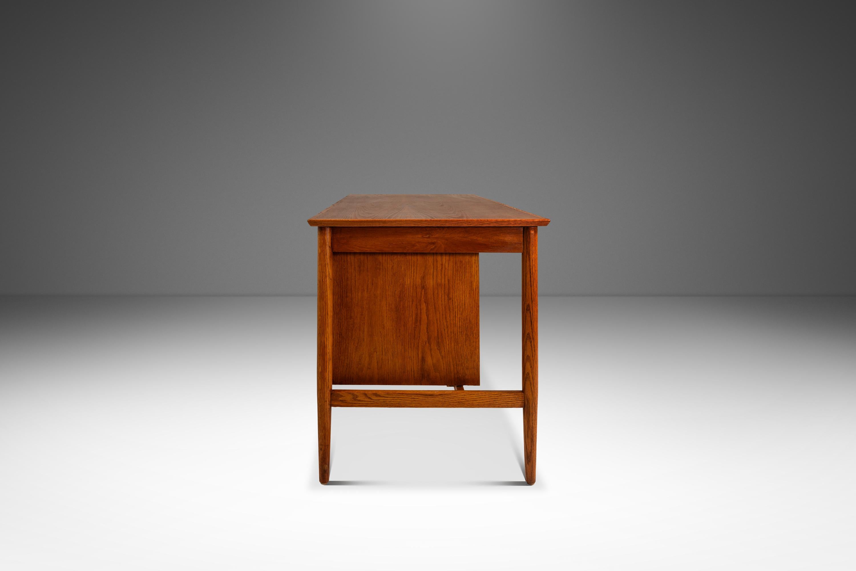 This exquisite Mid-Century Danish Modern writer’s desk, attributed to Arne Vodder for H. Sigh & Son, embodies the refined simplicity of 1960s Scandinavian design. Crafted from solid oak, the desk features a warm, natural finish that highlights the