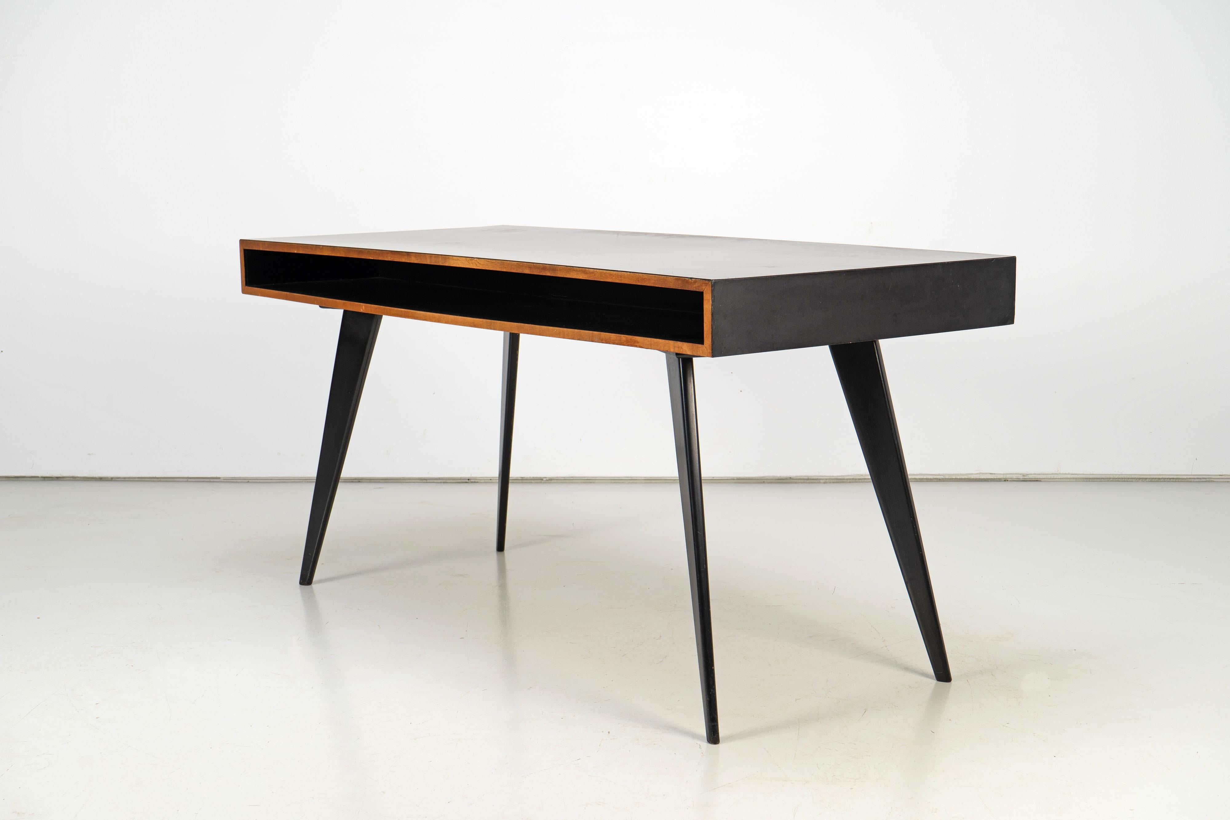Schreibtisch, entworfen von Hans Bellmann in den 1950er Jahren. Die Schreibtischplatte besteht aus Ahornholz und schwarzem Formica und hat auf beiden Seiten Ablagen. Die spitz zulaufenden Holzbeine sind mit schwarzem Lack überzogen.