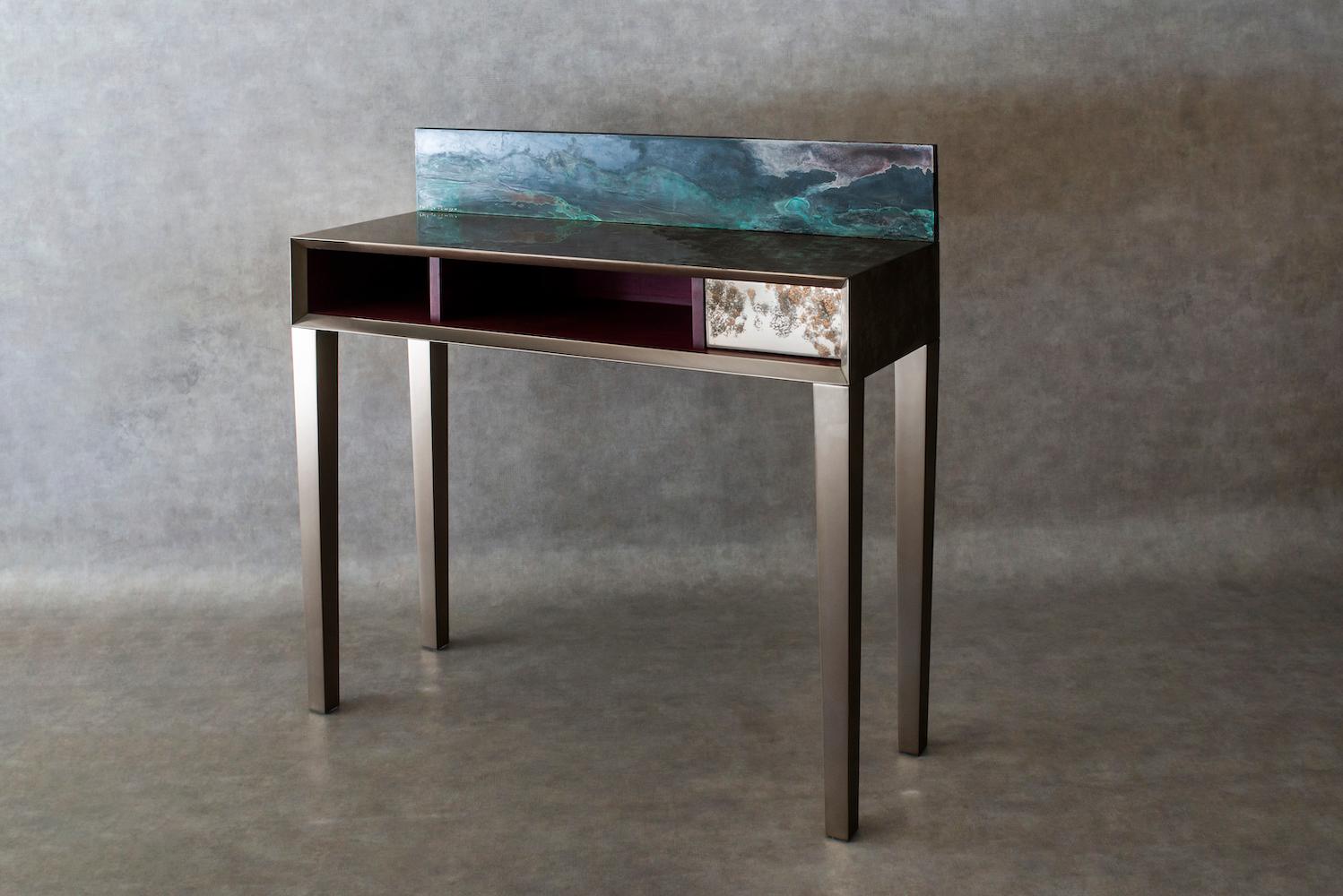 This writing desk is fully clad in titanium, except for the storage space whose two small compartments are crafted from amaranth, a precious hardwood known for its purple hue. A removable top makes it easy to switch up the decor: the flip side is a