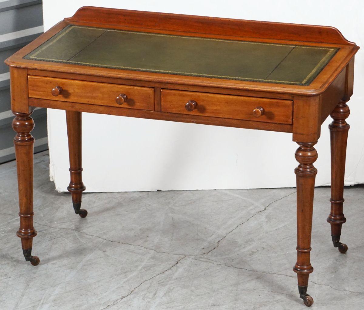 A handsome English writing table or desk of mahogany from the 19th century, featuring a leather top embossed with gilt edge, with shaped gallery back, over a frieze of two fitted drawers - each with two turned knob pulls, and resting on turned legs