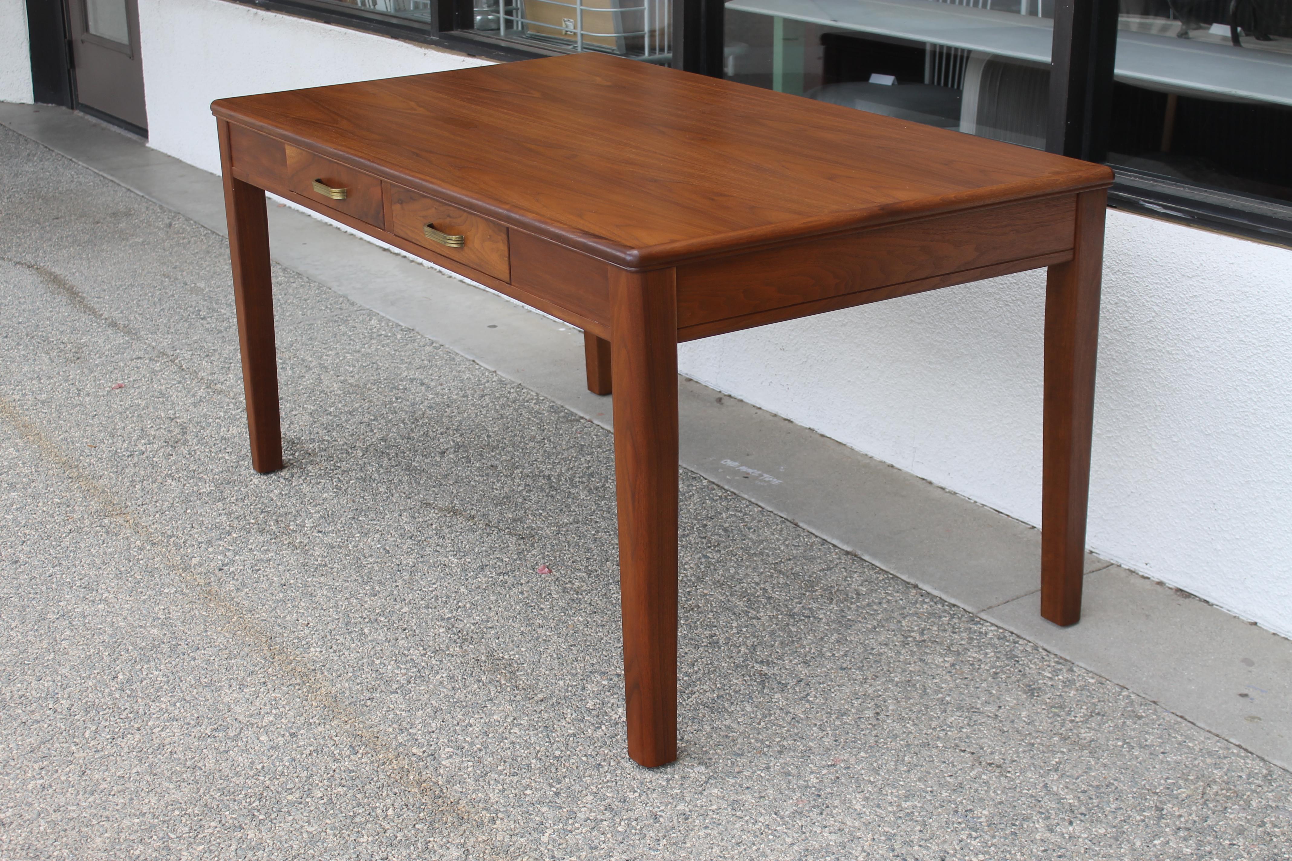 A Mid-Century Modern walnut writing table or desk made by the Leopold Company with two drawers and brass hardware. Paper label attached stating The Leopold Company, Burlington, Iowa U.S.A. Table has been professionally refinished. Table measures 60