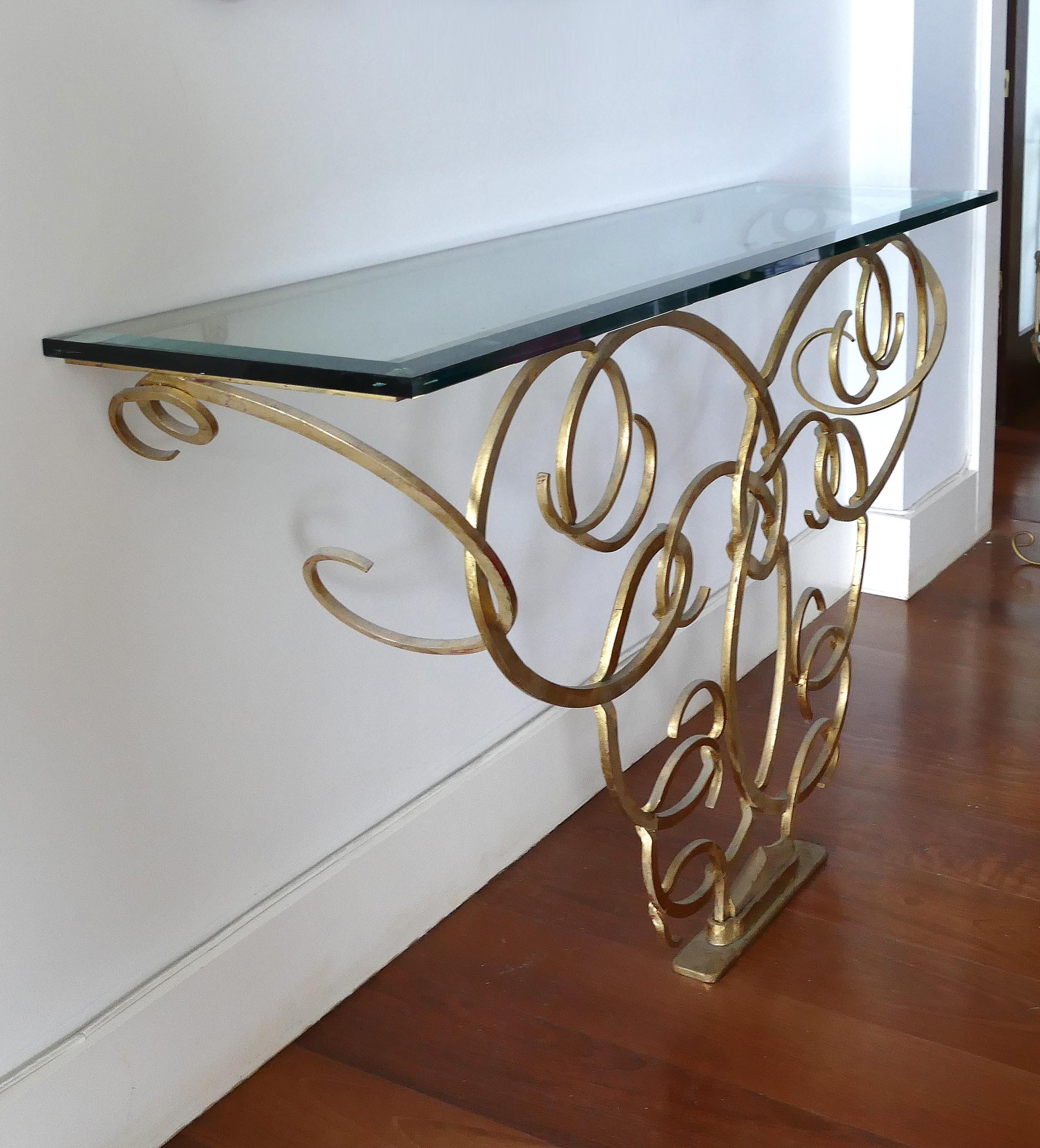 Wrought gilt iron console after Raymond Subes with glass top 

Offered for sale is a handwrought sculptural gilt iron console table with a glass top in the manner of Raymond Subes. The ironwork evokes a sense of lightness with great movement; the