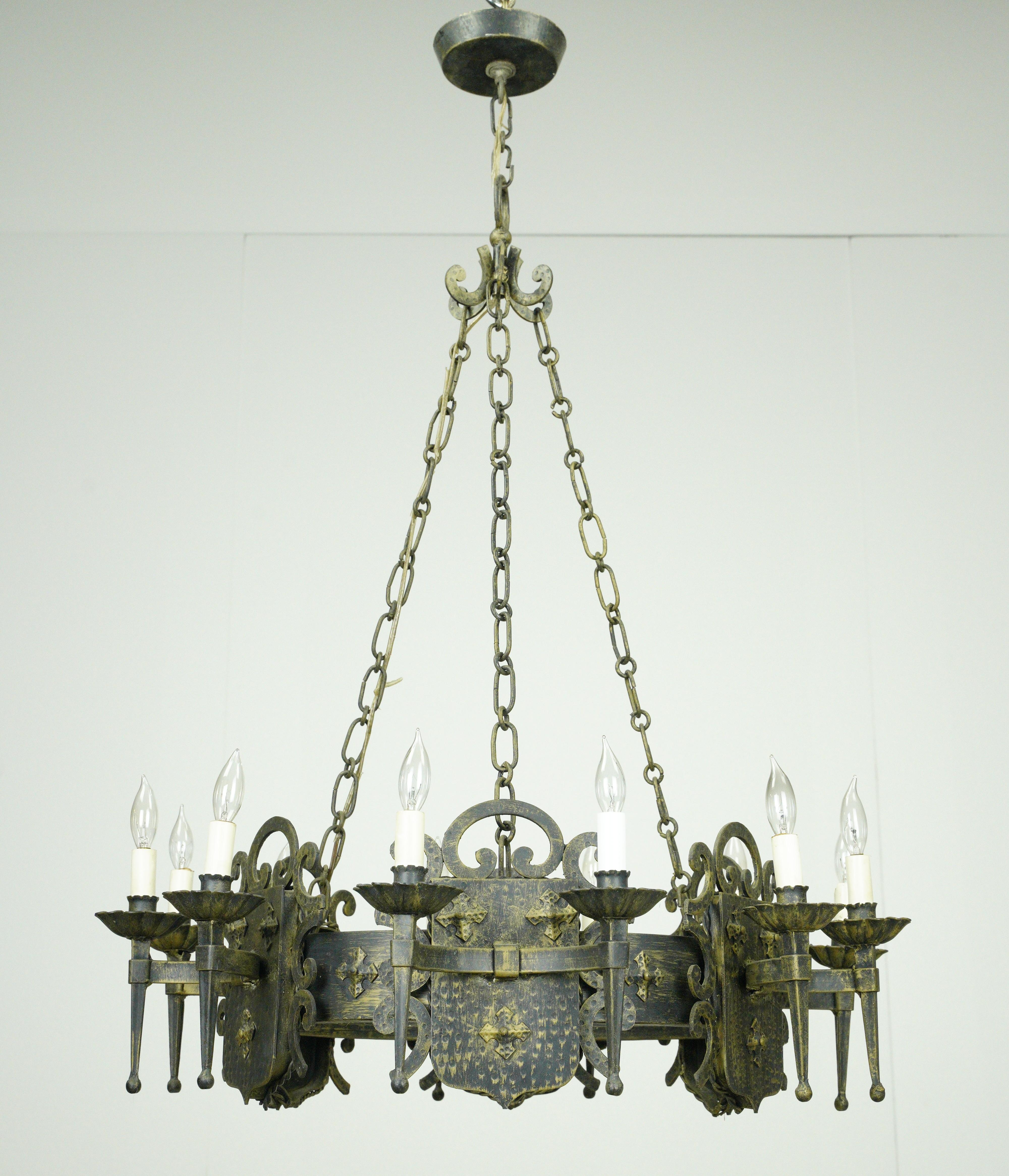 Realizzato in ferro battuto, questo lampadario emana un'estetica medievale, con il ferro grezzo che mette in mostra la bellezza delle finiture rovinate. Caratterizzato da dodici bracci disposti a scudo, ciascuno impreziosito da dettagli a voluta,
