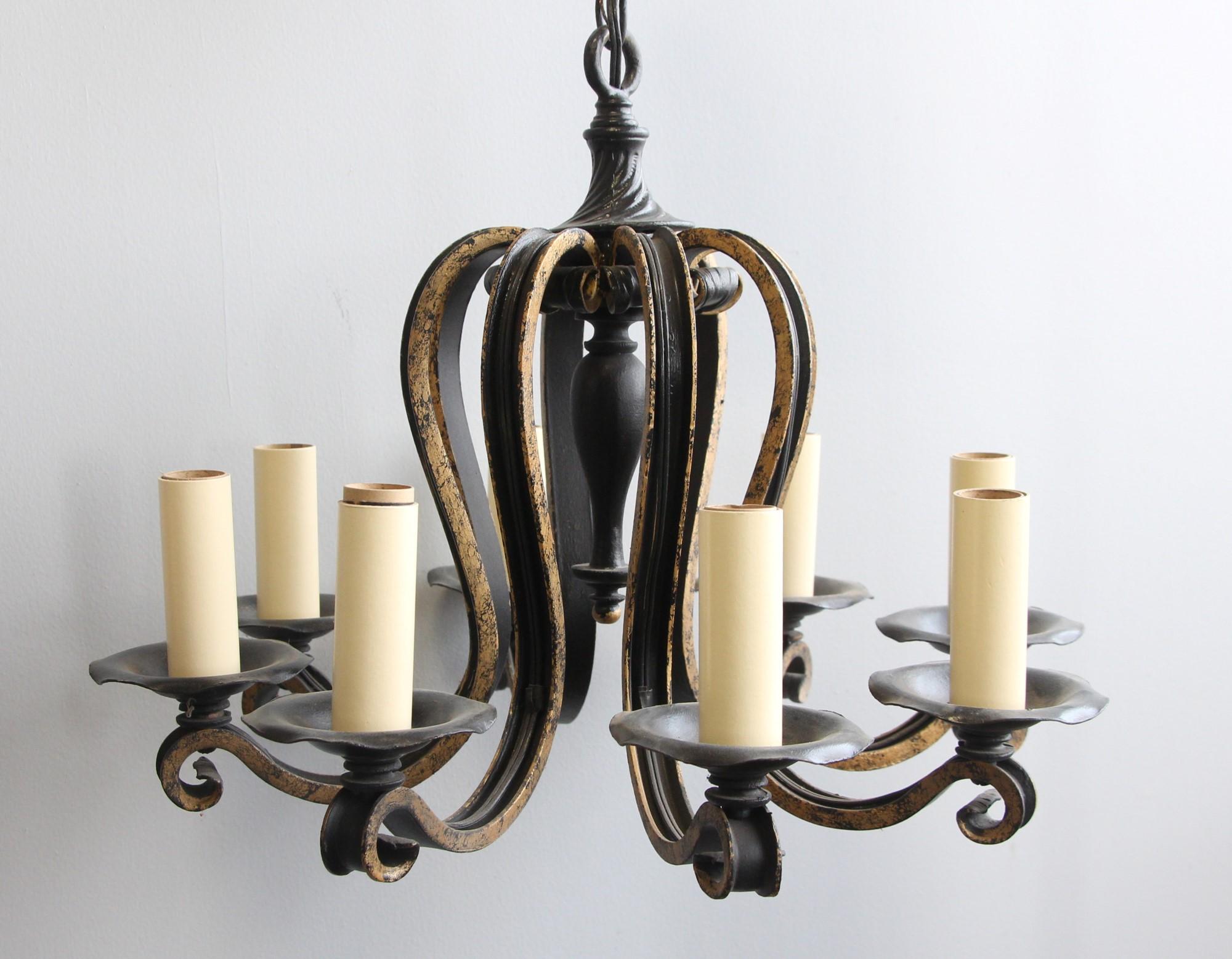 Unique early 20th century wrought iron eight arm chandelier with gold painted arms. Reminiscent of a floral style with graceful sweeps out to each individual candelstick arm. This can be seen at our 1800 South Grand Ave location in Downtown LA.
