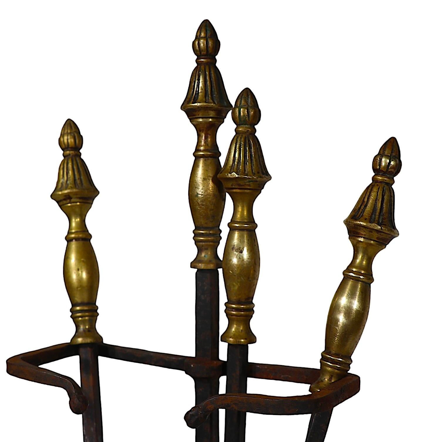 Four piece wrought iron and cast brass fireplace tool set, including a poker, shovel, tongs, and the stand. The set is in good, original, clean and ready to use condition, showing some  cosmetic wear to its surface, normal and consistent with age. 