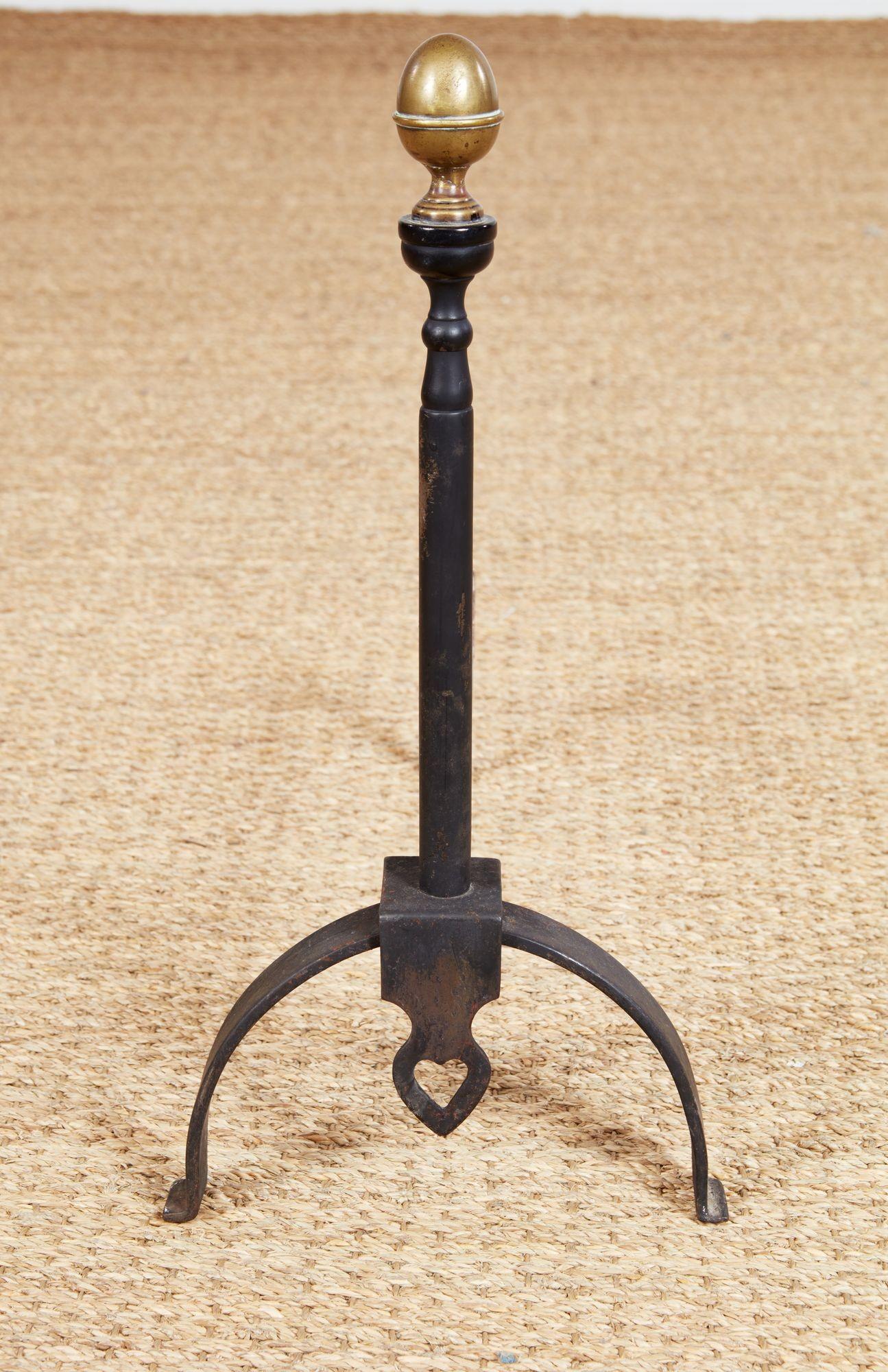 A pair of blacksmith-made andirons featuring drop finials with pierced heart decoration, wide arched legs and turned iron shafts surmounted by bronze acorn finials. English, circa 1900.