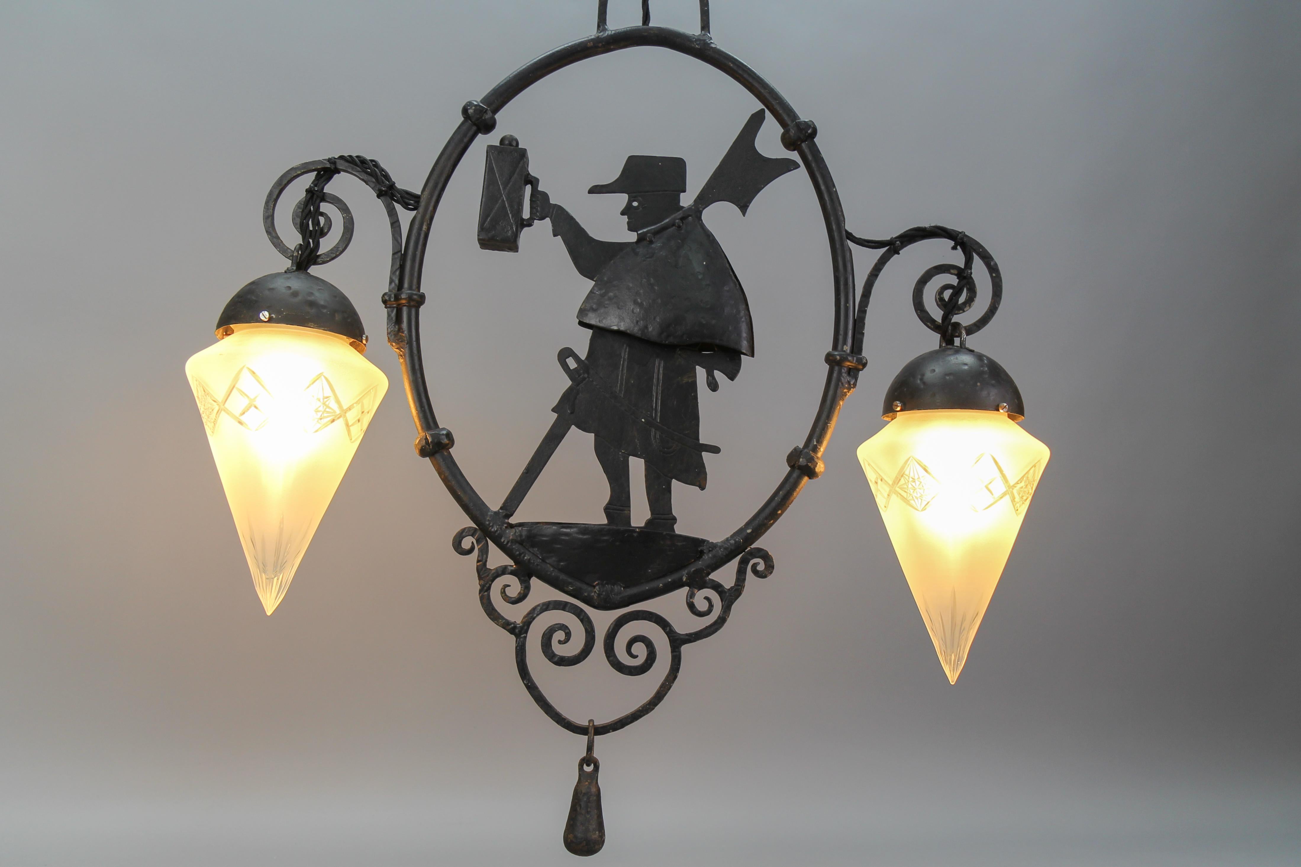 Wrought iron and cut frosted glass two-light pendant chandelier with night watchman, from ca 1910.
Gorgeous masterfully crafted wrought iron pendant chandelier with a night watchman figure and two beautiful white cone-shaped cut frosted glass