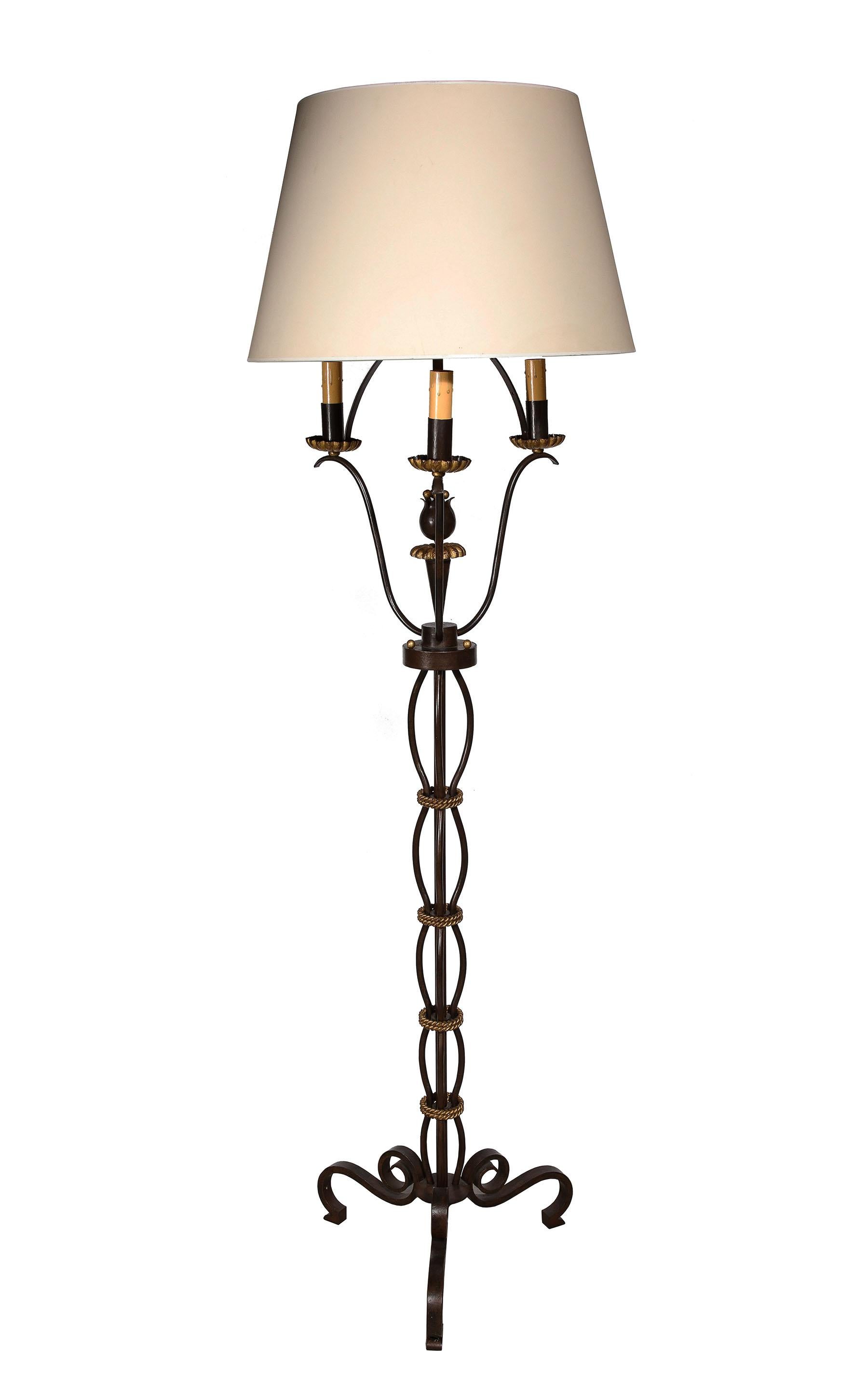 The wrought iron floor lamp with a sculpted tulip figure to center and gilt bronze rope wrapped stem, having three lights supported by scrolling arms ending in tole bobeches all on a tripod base.