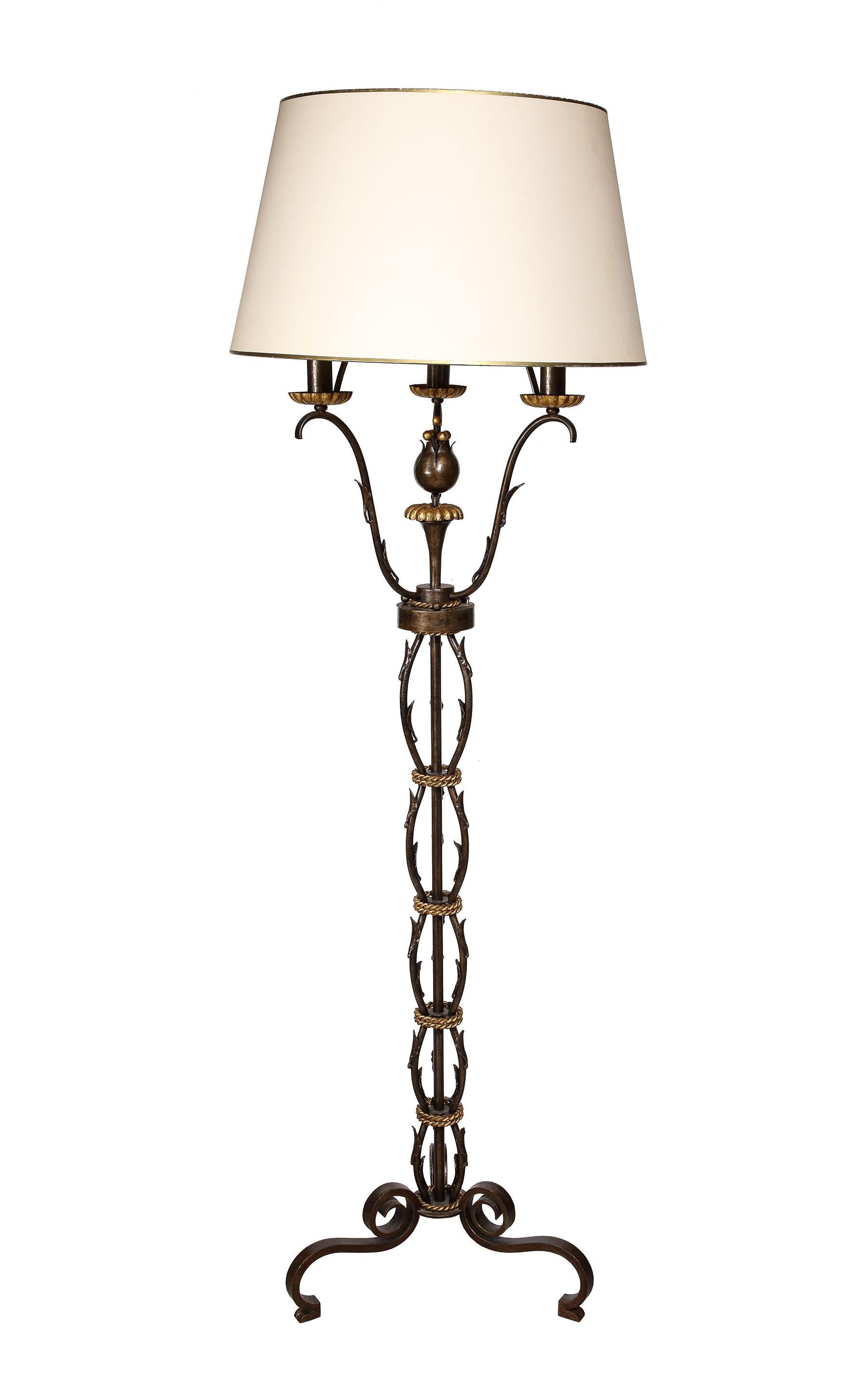 The wrought iron floor lamp with a sculpted tulip figure to center and gilt bronze rope wrapped stem, having three lights supported by scrolling arms ending in tole bobeches all on a tripod base.