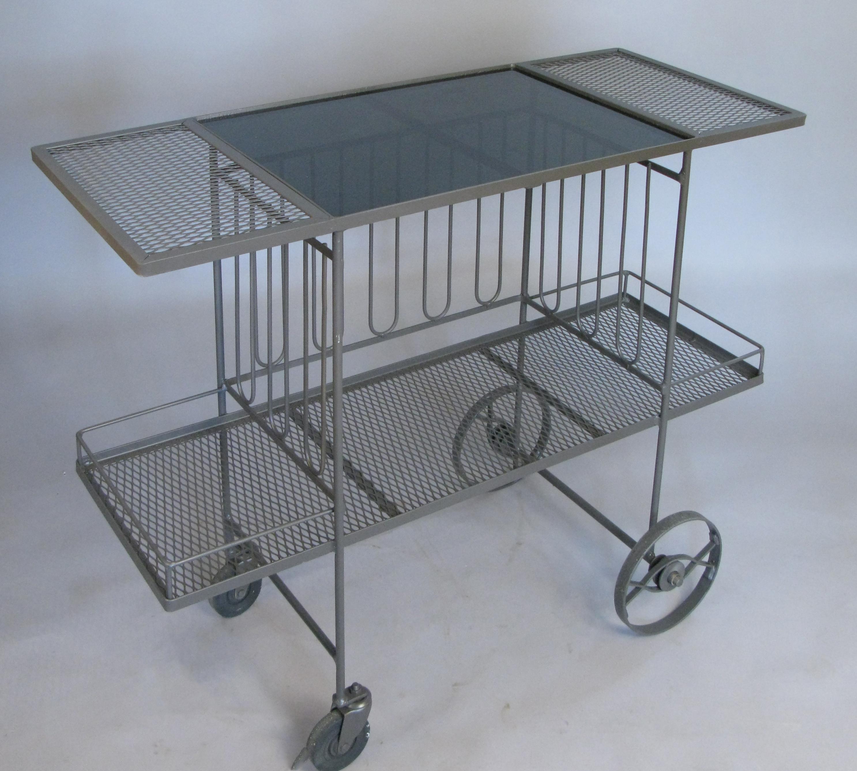 A very nice 1950s rolling bar cart in wrought iron with long vertical details around the center section, lower shelf with gallery rail, and a smoked black glass top, by Salterini.