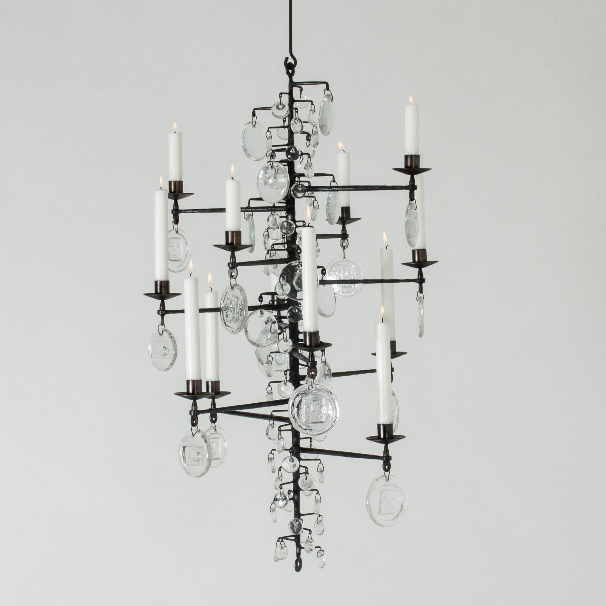 Stunning candle chandelier by Erik Höglund, made from wrought iron and glass. The long, rustic iron frame is adorned with different sized glass medallions that look like large rain drops on a bare tree. The biggest medallions are embossed with