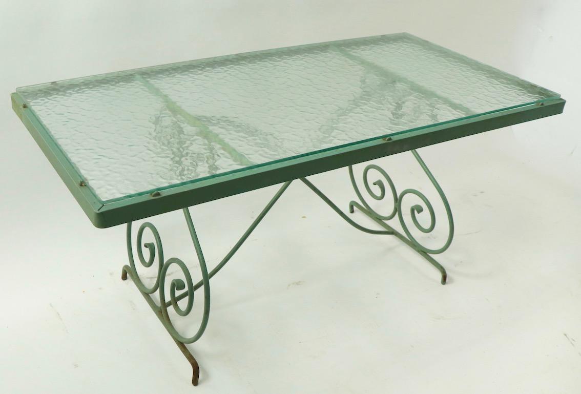 Chic and stylish wrought iron coffee table by Woodard. Rectangular textured glass top with scrolled metal legs, glass top has a stain, probably from a plant. Originally designed for a patio suitable for both indoor and outdoor. Glass usable as is or
