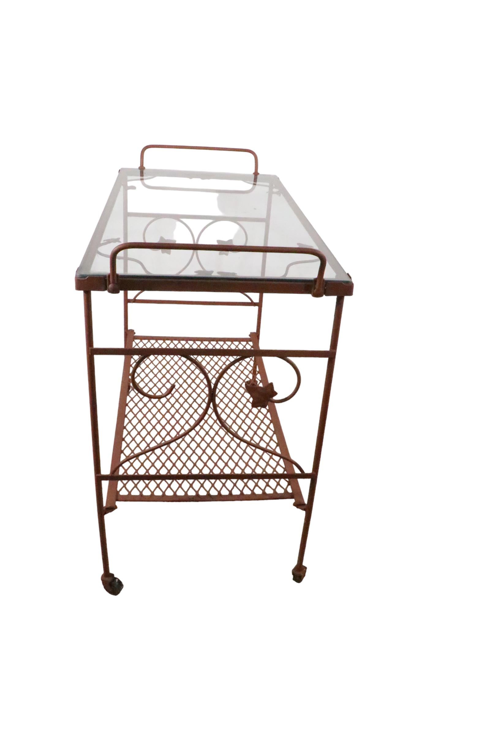 Joli chariot de service et de bar surdimensionné en fer forgé, maille métallique et verre. Le chariot a deux étagères ( 29.5 H x 9 H in. ) il est sur roues, et est en très bon état, propre, d'origine. Une feuille décorative en métal moulé est