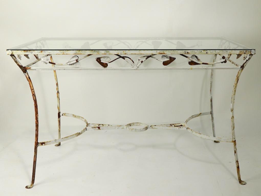 Nice diminutive wrought iron and glass dining having metalwork foliate trim, penny feet and original plate glass top. The center stretcher features a plant holder (diameter 5 inch) as shown. The table is in old rust finish, use as is, or we can