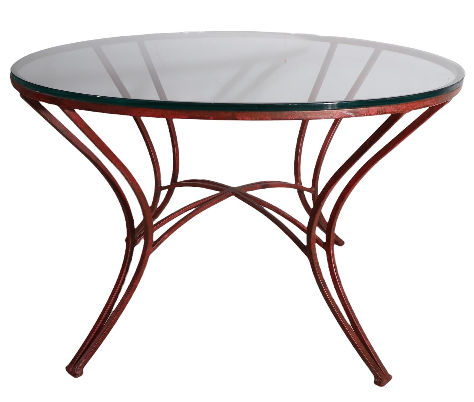 Stylish round side, or end table having an exaggerated and dramatic wrought iron base in intriguing Chinese red paint finish, with a thick plate glass top. The table is in very good, clean, original condition, showing only light cosmetic wear,