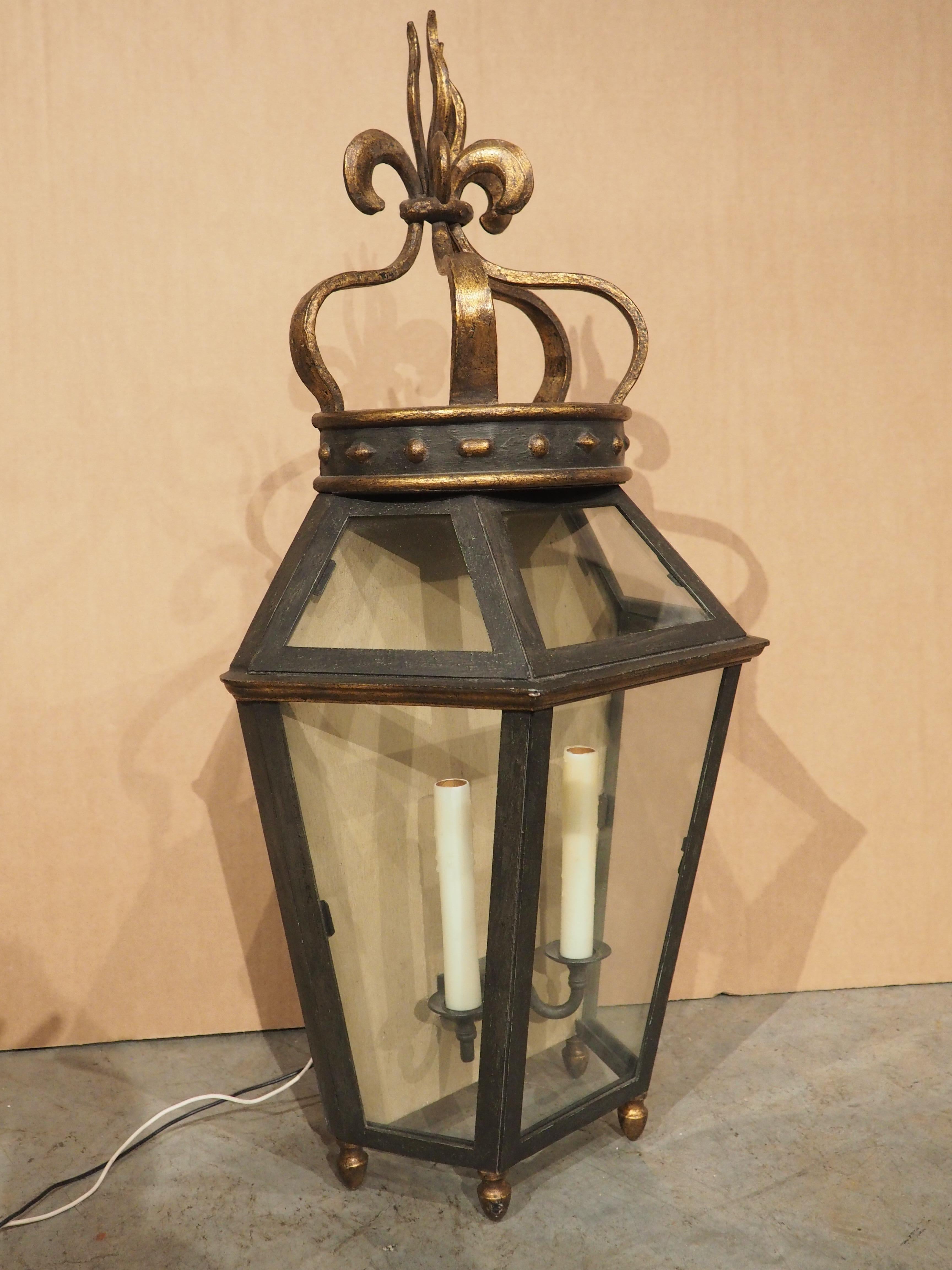 A fascinating wall lantern that can be paired with just about any architectural style from country French to Italian Renaissance. The wrought iron and glass lantern has a half-hexagon main body comprised of six panes of glass that encase two white