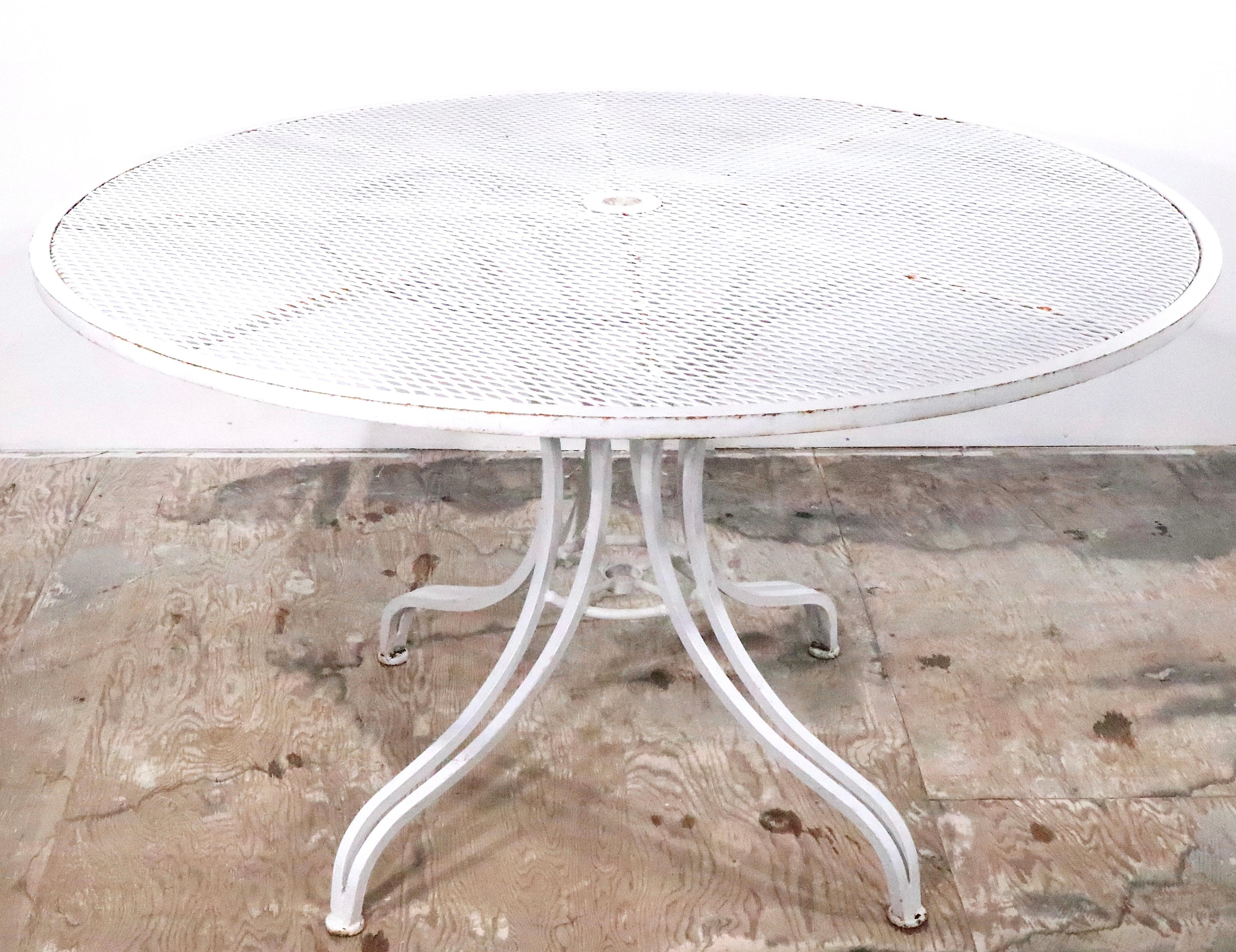 Exceptional vintage garden, patio, poolside table of wrought iron and metal mesh. The table features a stylized architectural pedestal base of heavy gauge wrought iron, which supports the circular metal mesh top. This example is in very good