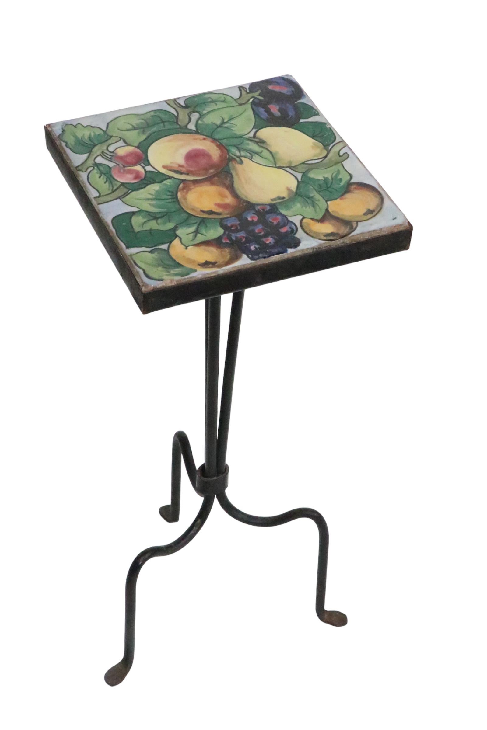 Charming wrought iron base, tile top occasional table, or  plant stand, design attributed to Addison Mizner. The table features a three rod base, which gathers and the bottom, and opens to three footed legs. The handprinted ceramic  tile top is a
