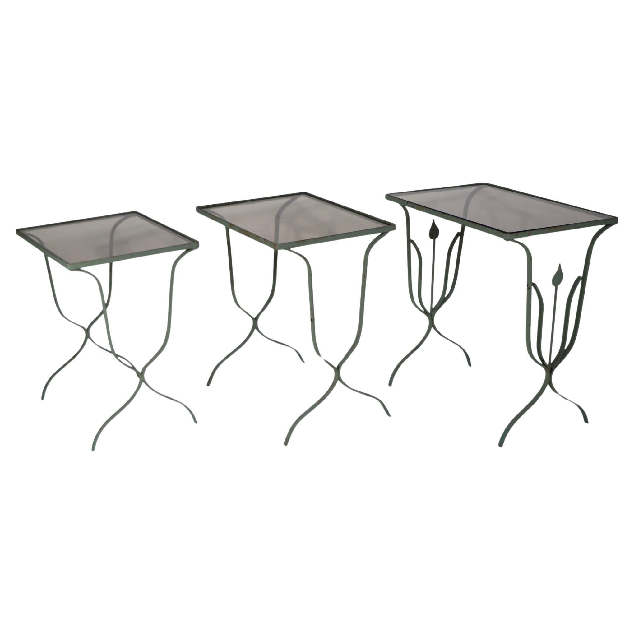 Unusual set of three graduated nesting  wrought iron and glass nesting tables. These chic tables feature an Art Deco  stylized modernist  profile of a plant on the largest table, and tinted, or smoked gray glass tops. The finish is original dusky