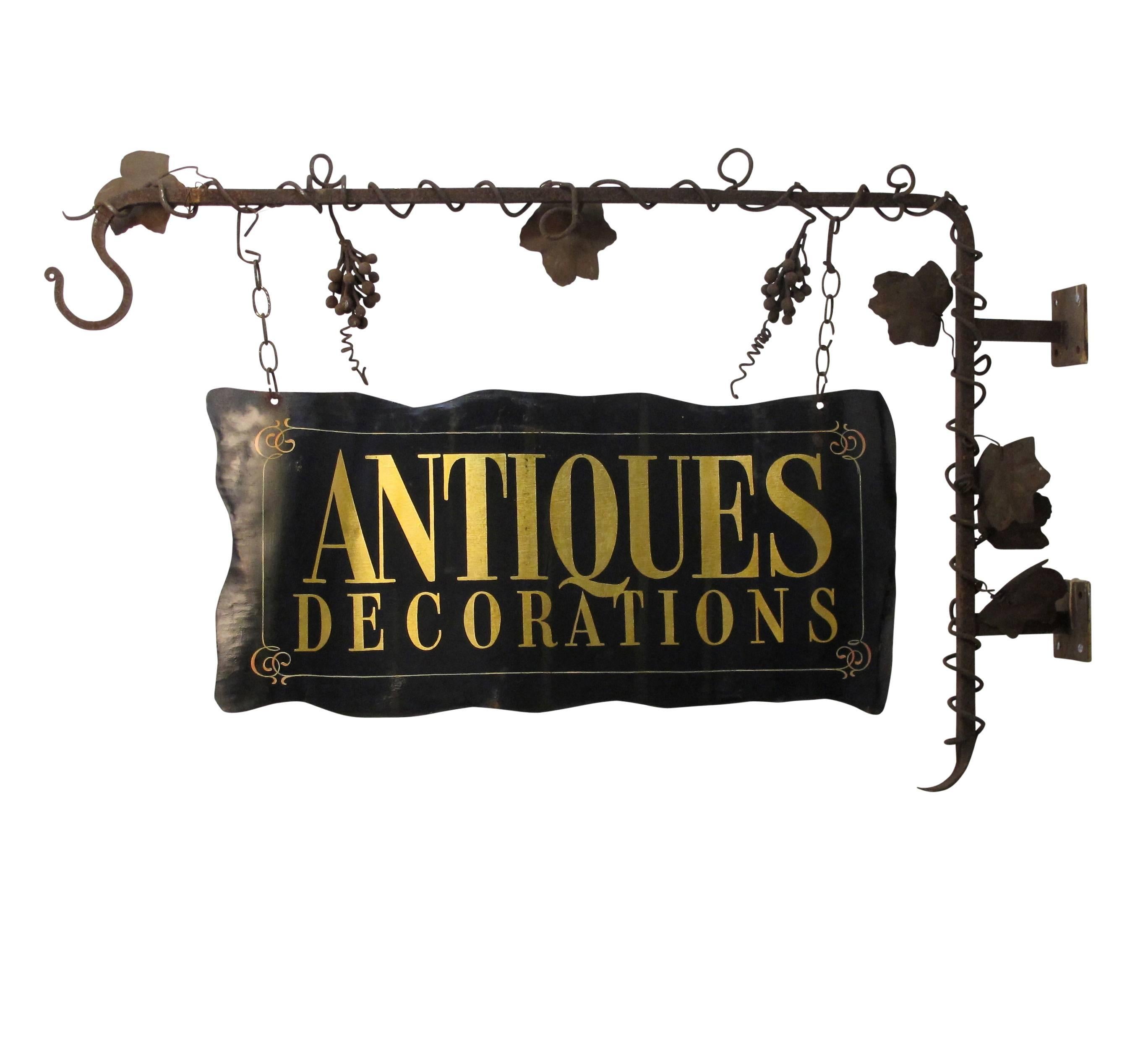 Large tole painted black and gilt ANTIQUES sign (double-sided) hanging from a hand-wrought iron hanger with twisting grape vine detail. Originally a wine store sign converted to an Antique Sign in the mid-20th century.
Measurements for just the